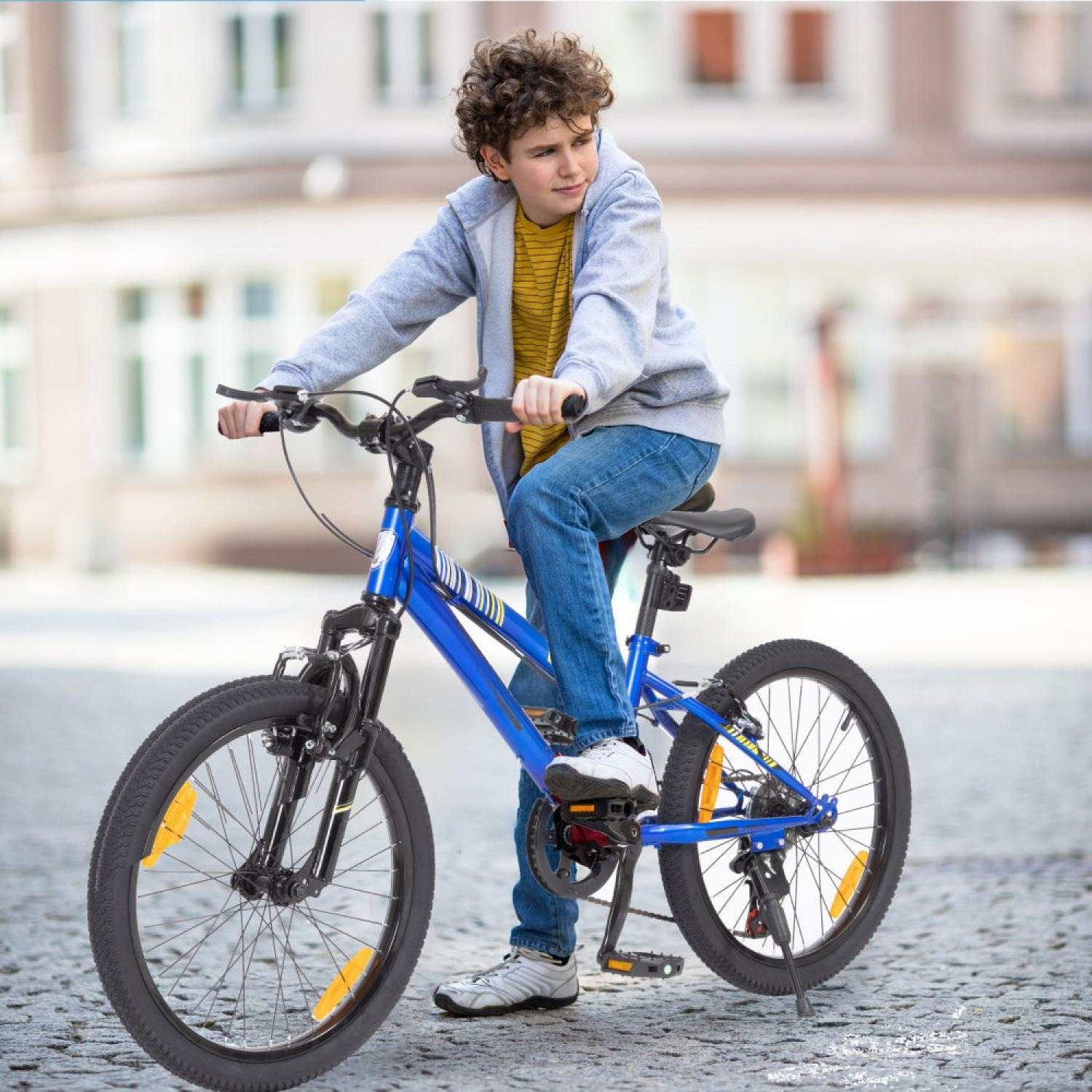 Ein Junge mit lockigem Haar sitzt auf einem blauen Fahrrad auf einer gepflasterten Straße.