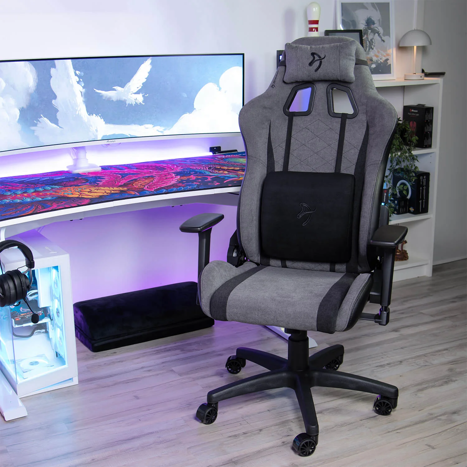 Een grijze gamestoel met lendekussen voor een grote gebogen monitor.