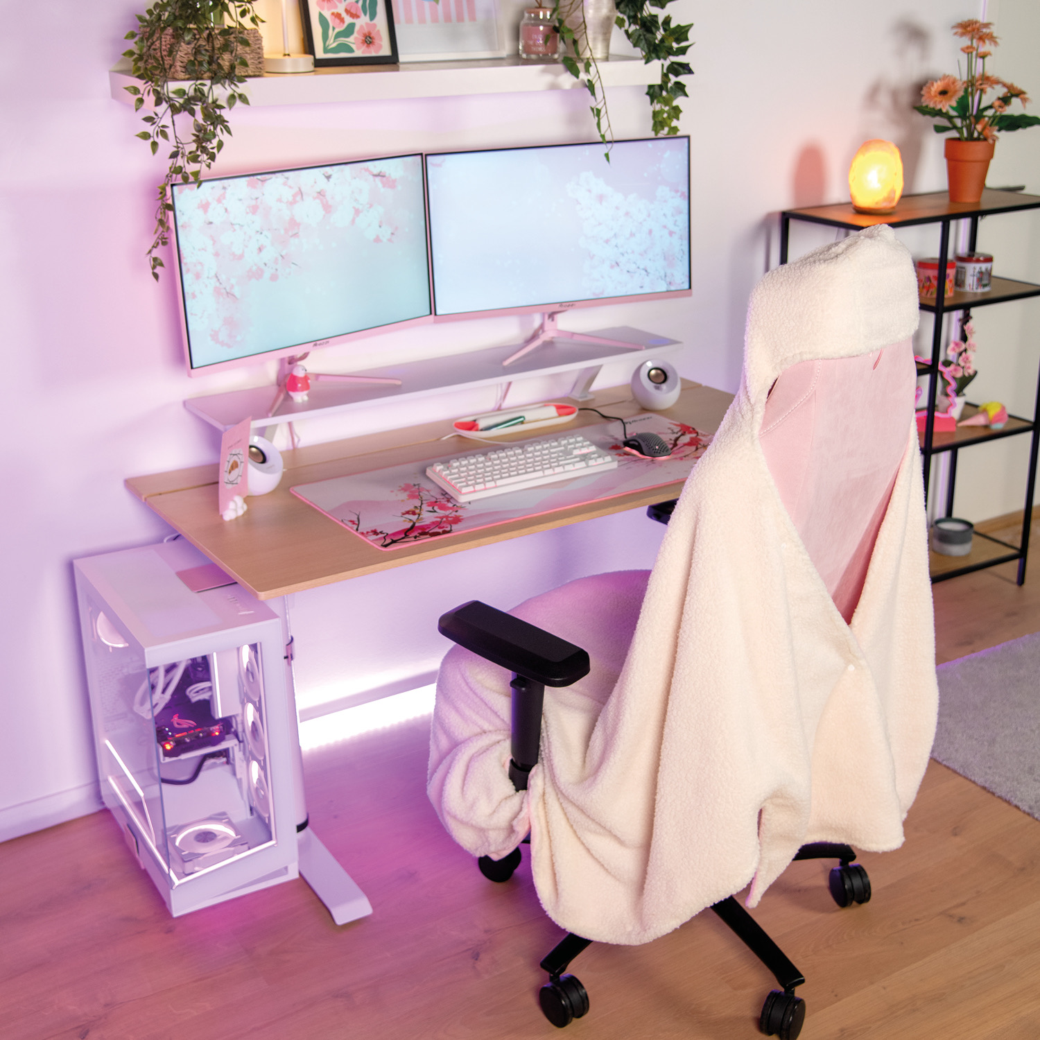 Una postazione gaming rosa con doppio monitor, tastiera, mouse e case PC bianco.