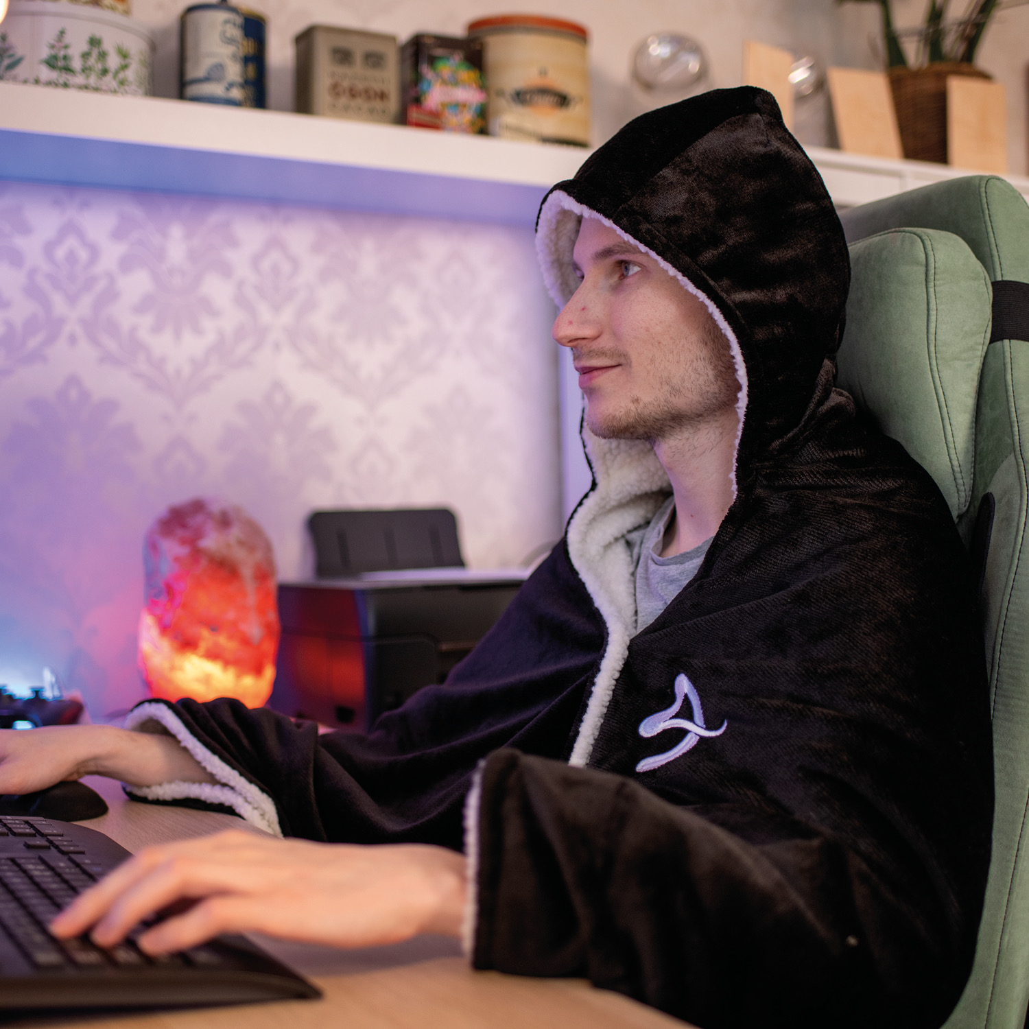 Uomo con mantella nera con cappuccio seduto al computer, luce di lampada di sale a sinistra.