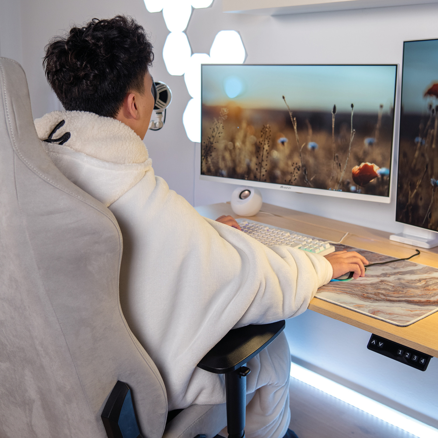 Uomo in felpa bianca seduto alla scrivania, gioca ai videogiochi su doppio monitor.