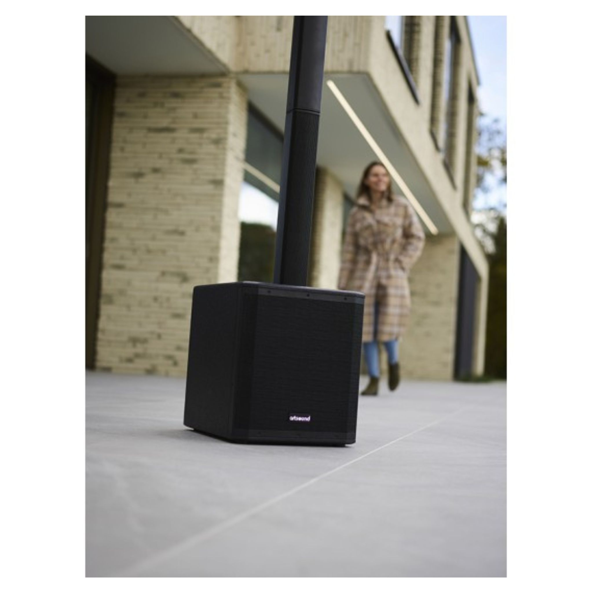 Enceinte noire avec colonne et femme en manteau à carreaux derrière.