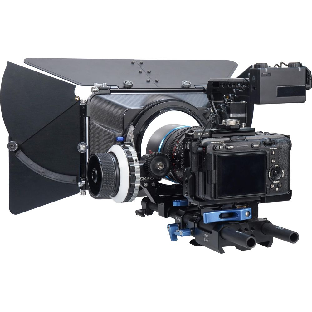 Eine professionelle Videokamera mit Objektiv, Matte Box und Zubehör auf weißem Hintergrund.