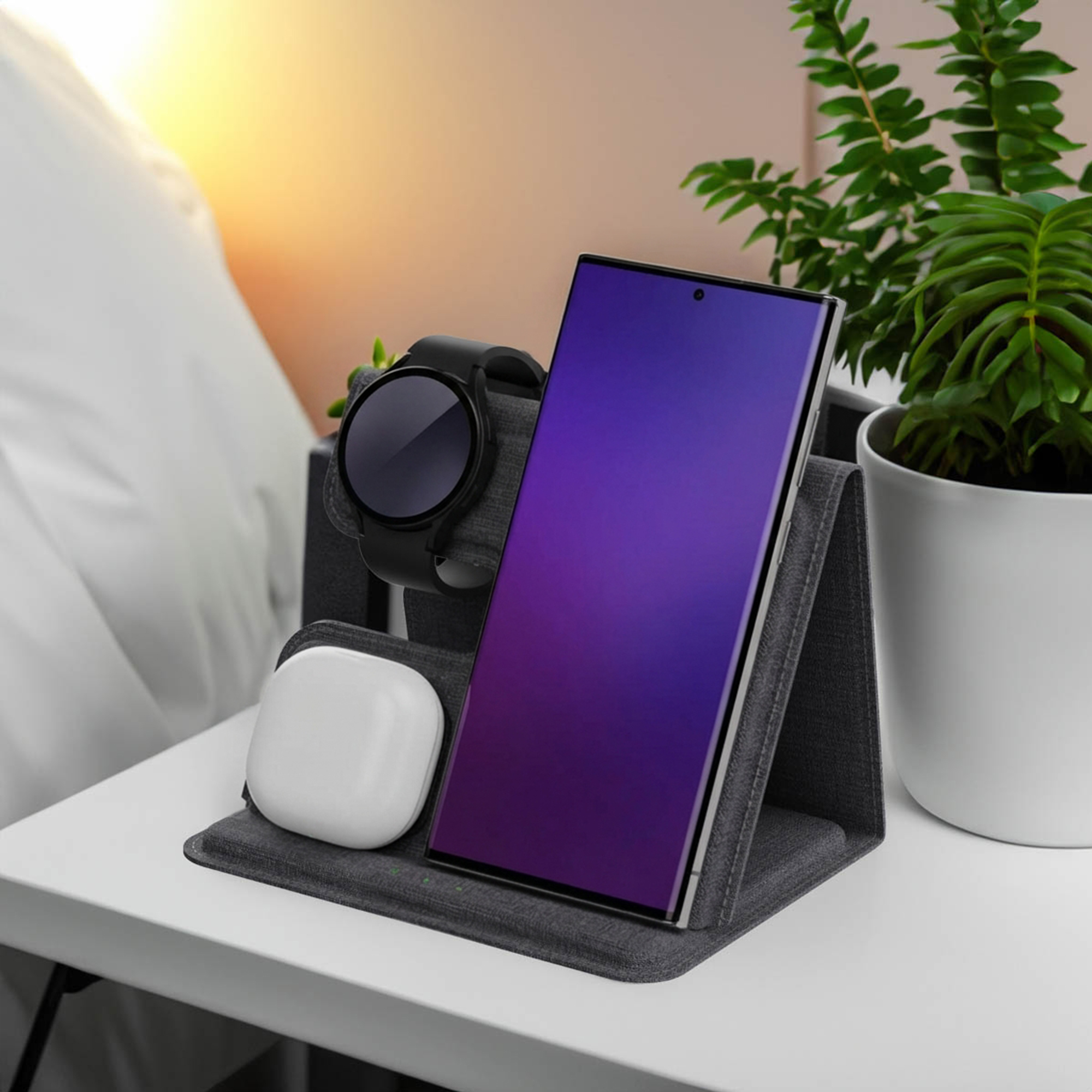 Een smartphone, smartwatch en oordopjes op een lader naast een plant.
