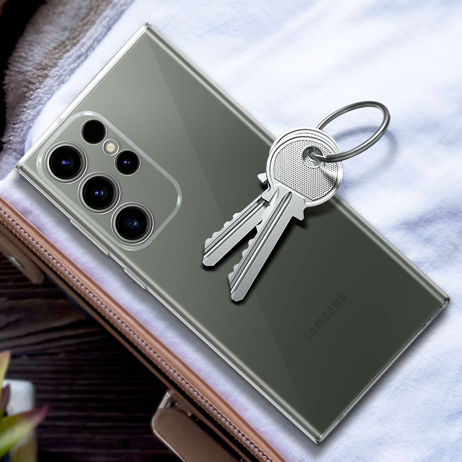 Een doorzichtige telefoonhoes met een Samsung telefoon en sleutels op witte stof.