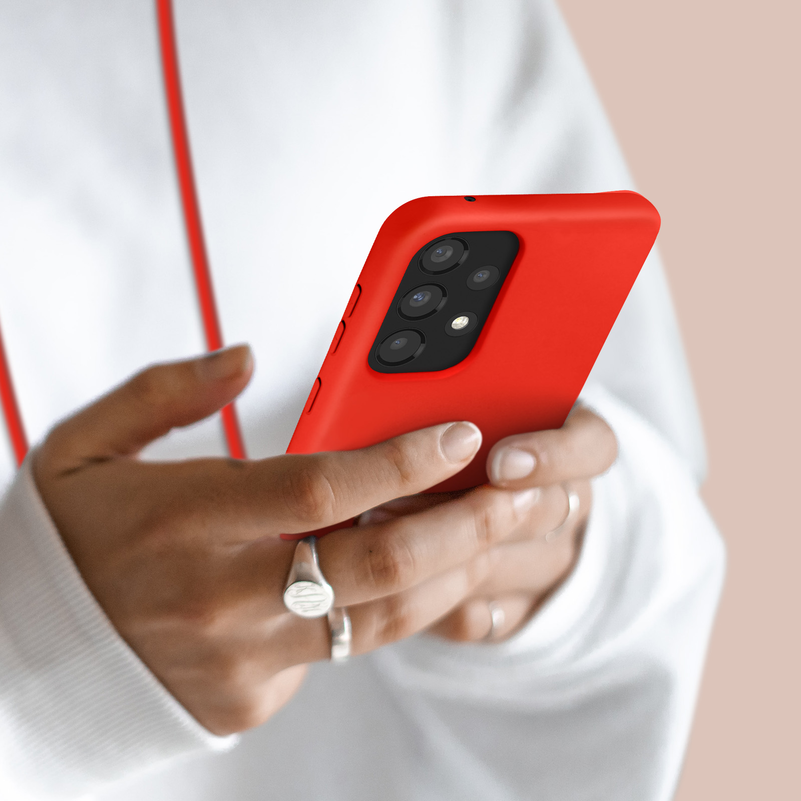 Une personne en sweat à capuche blanc tient un smartphone rouge avec quatre caméras.