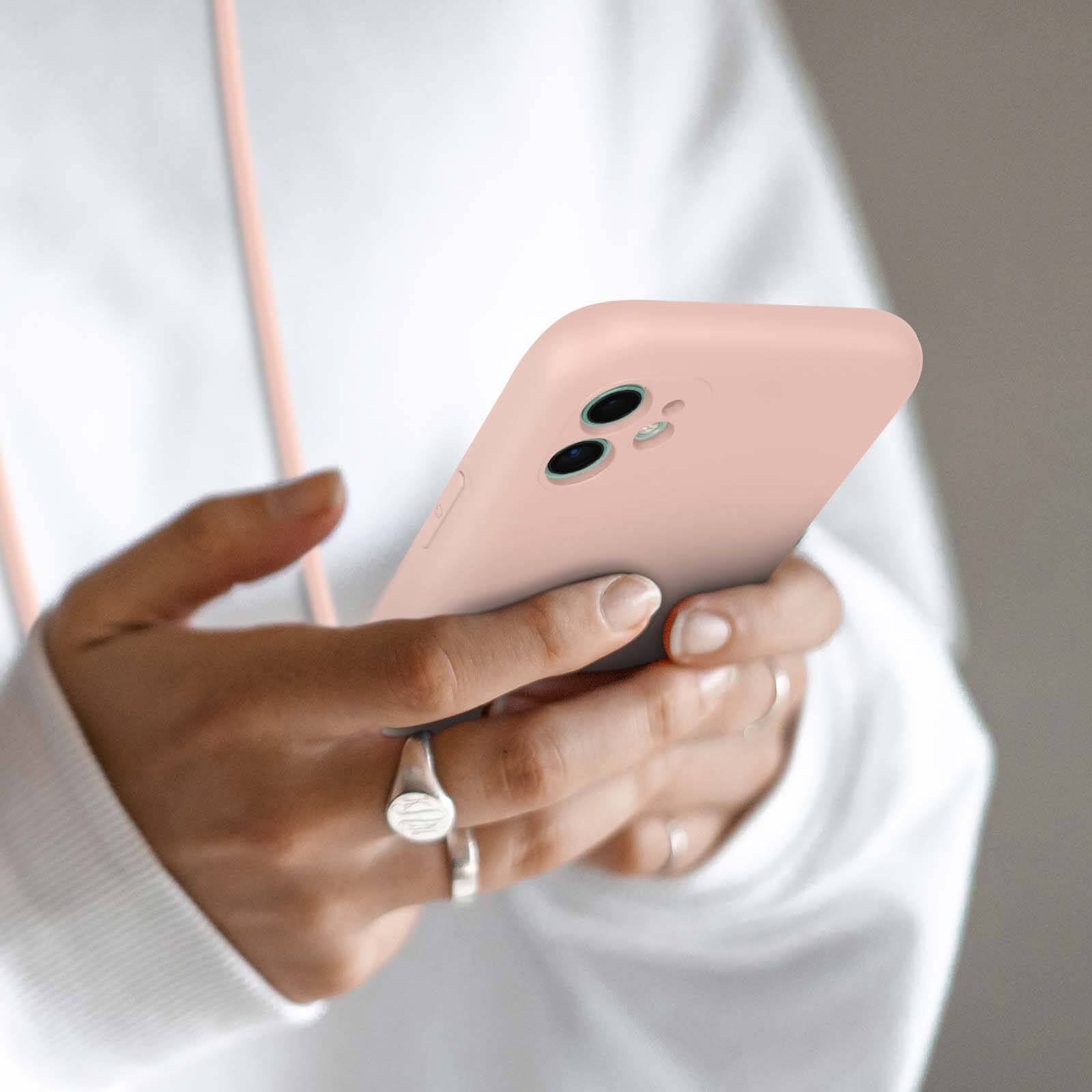 Mains tenant un iPhone rose à deux caméras. Une bague est visible.