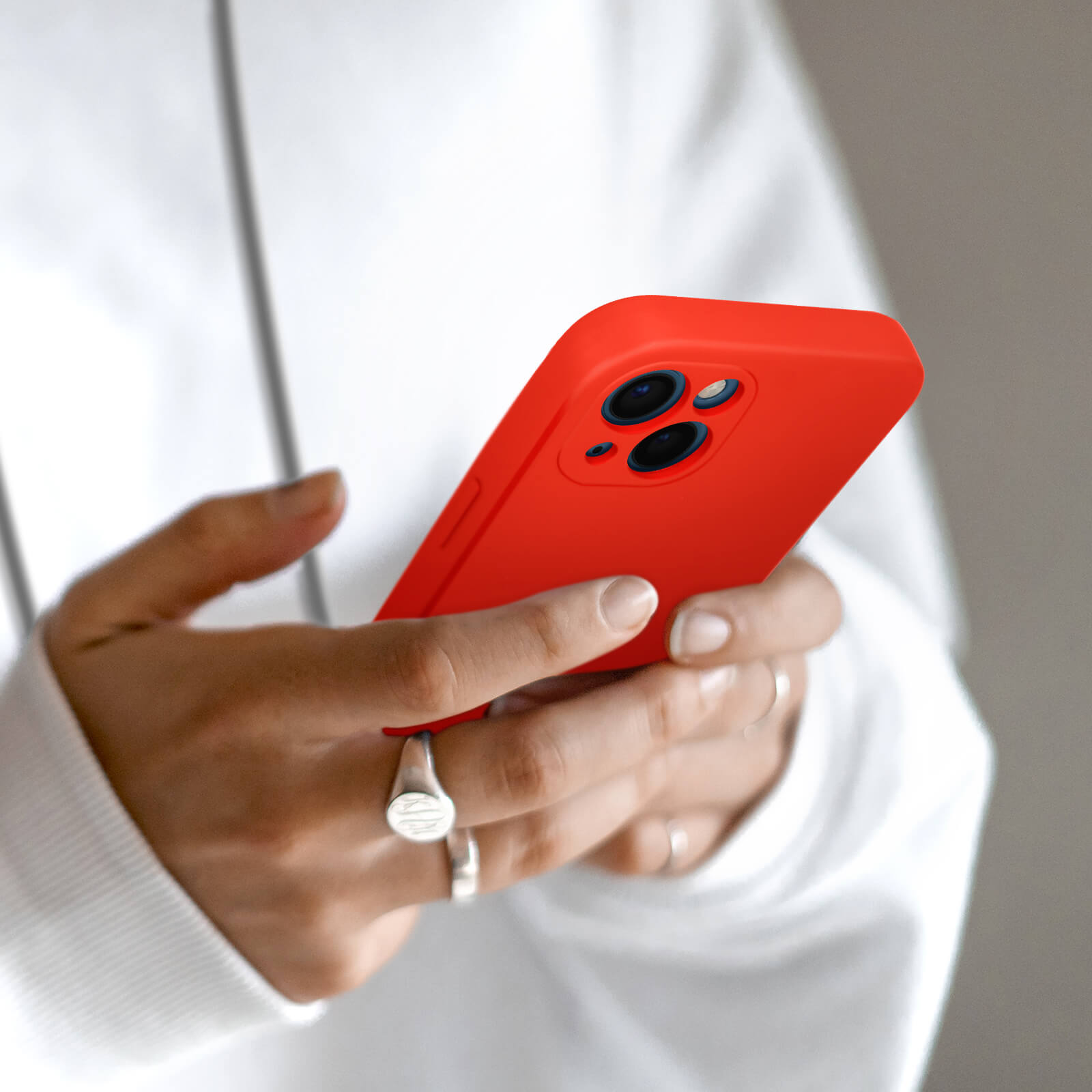 Handen houden een rode smartphone met drie cameralenzen vast.