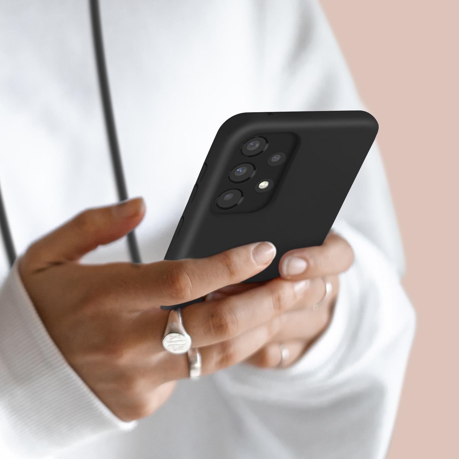 Une personne tient un smartphone noir avec quatre caméras. Elle porte un sweat blanc.