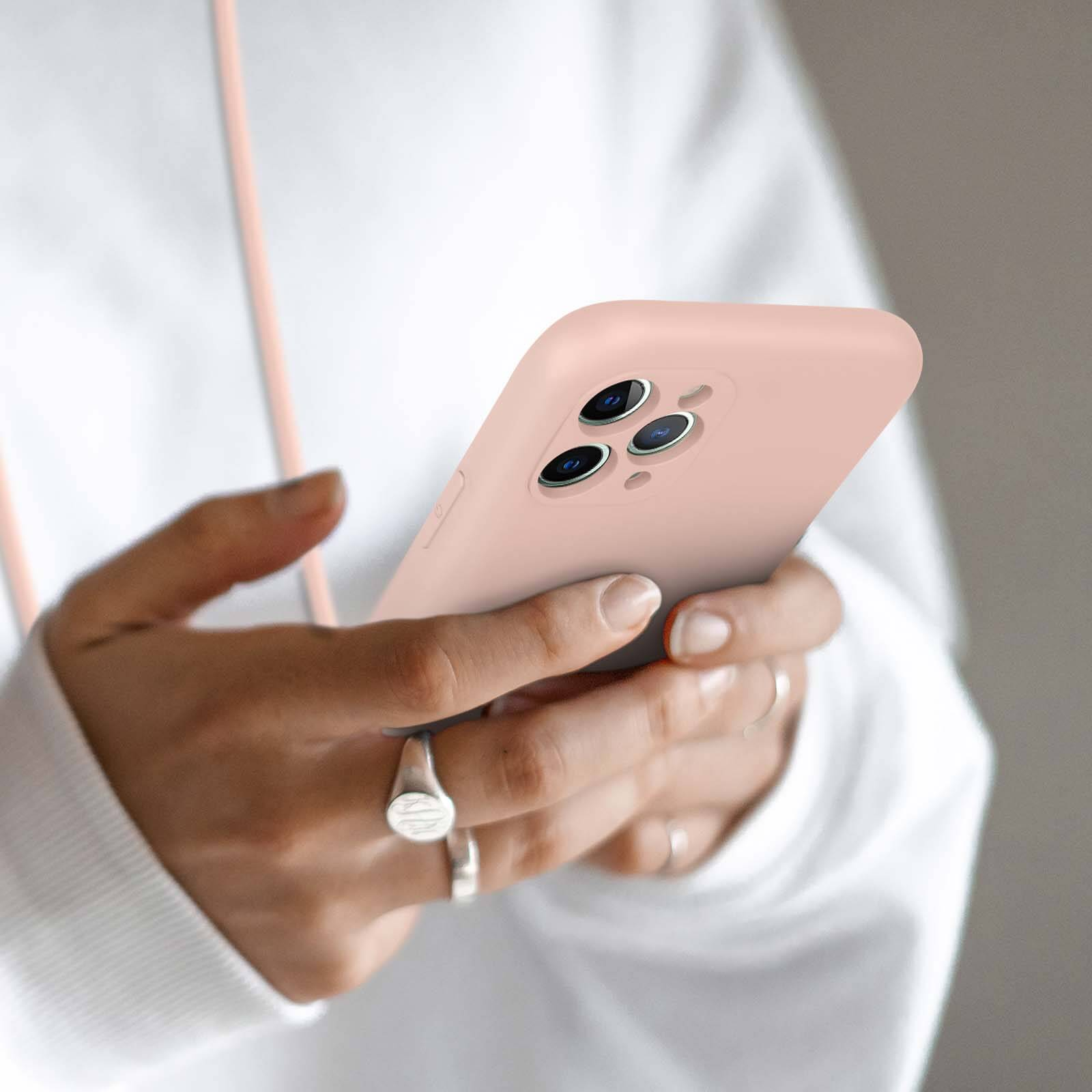 Mains tenant un smartphone rose avec trois objectifs de caméra.