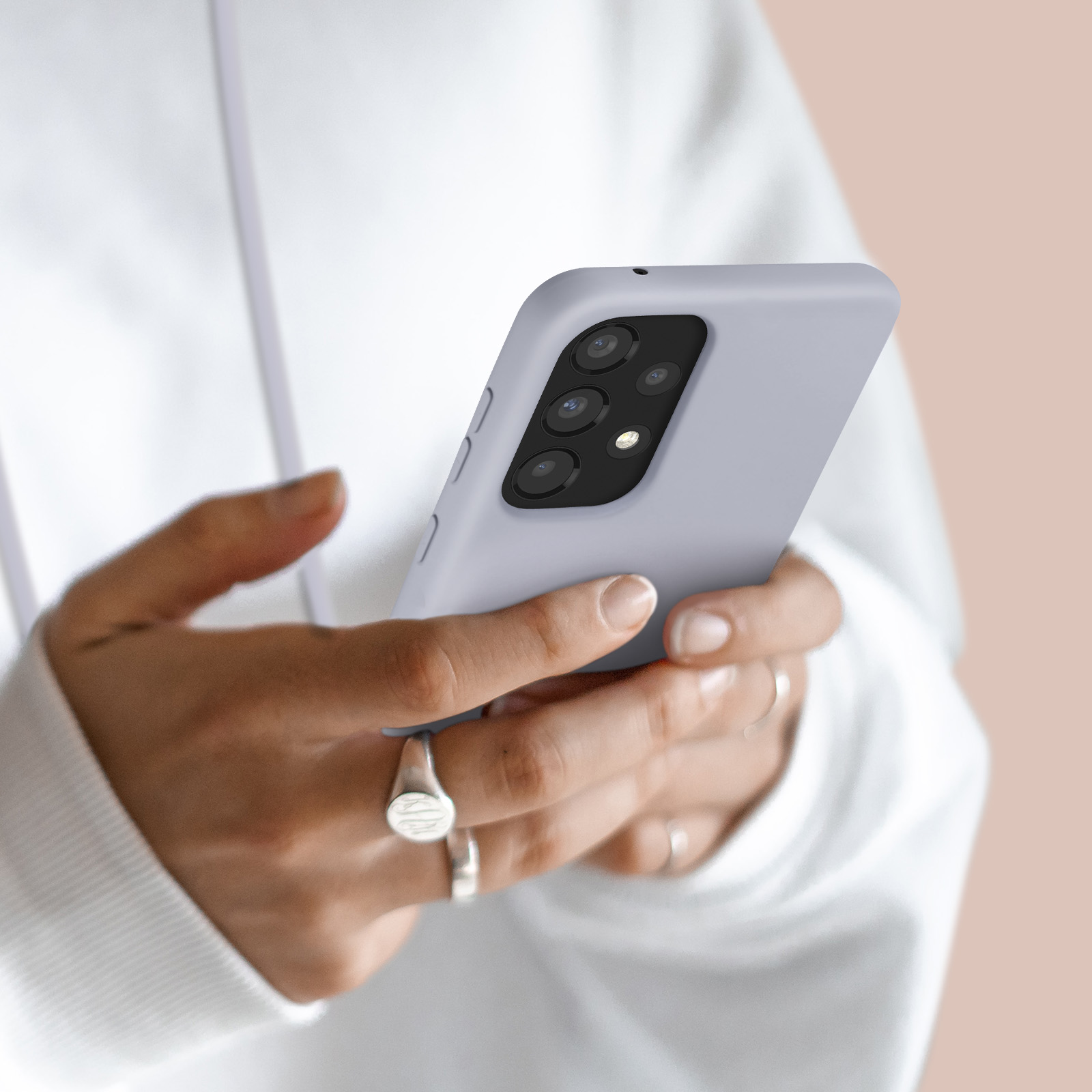 Une personne en sweat à capuche blanc tient un téléphone violet clair avec appareil photo multi-objectifs.