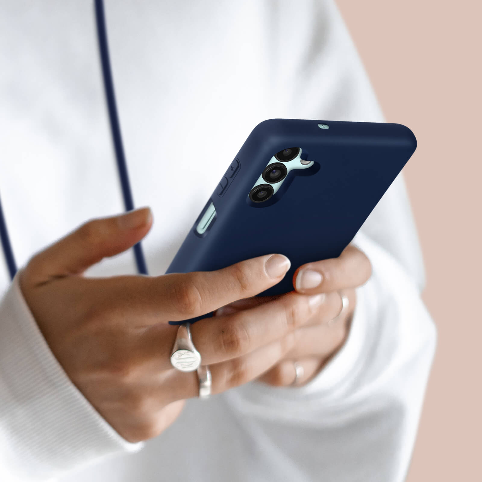 Gros plan des mains tenant un téléphone bleu foncé, associé à un sweat à capuche blanc.