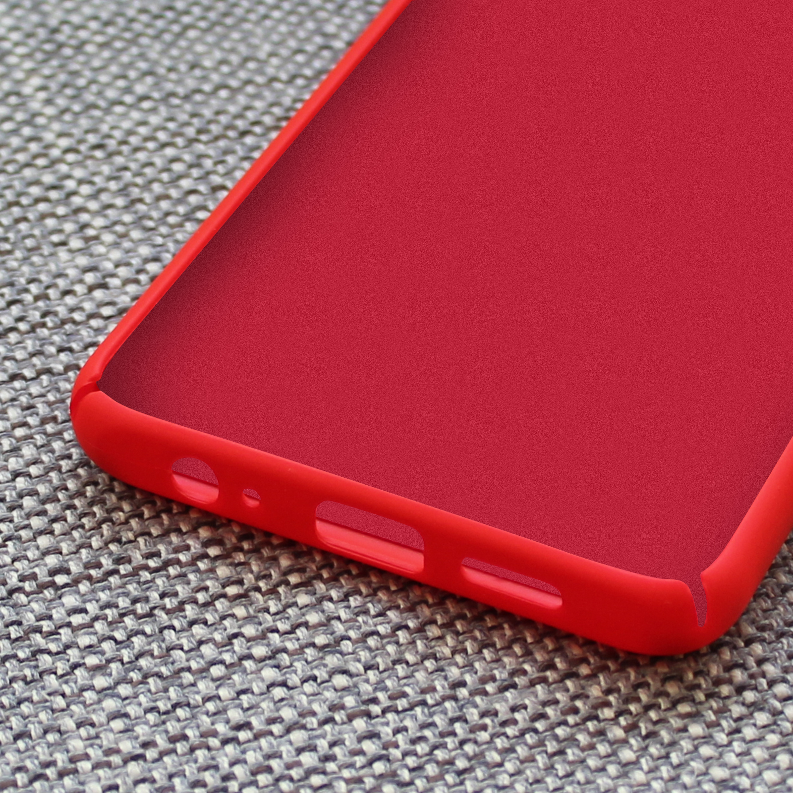 Coque de téléphone rouge avec découpes pour ports sur tissu gris.