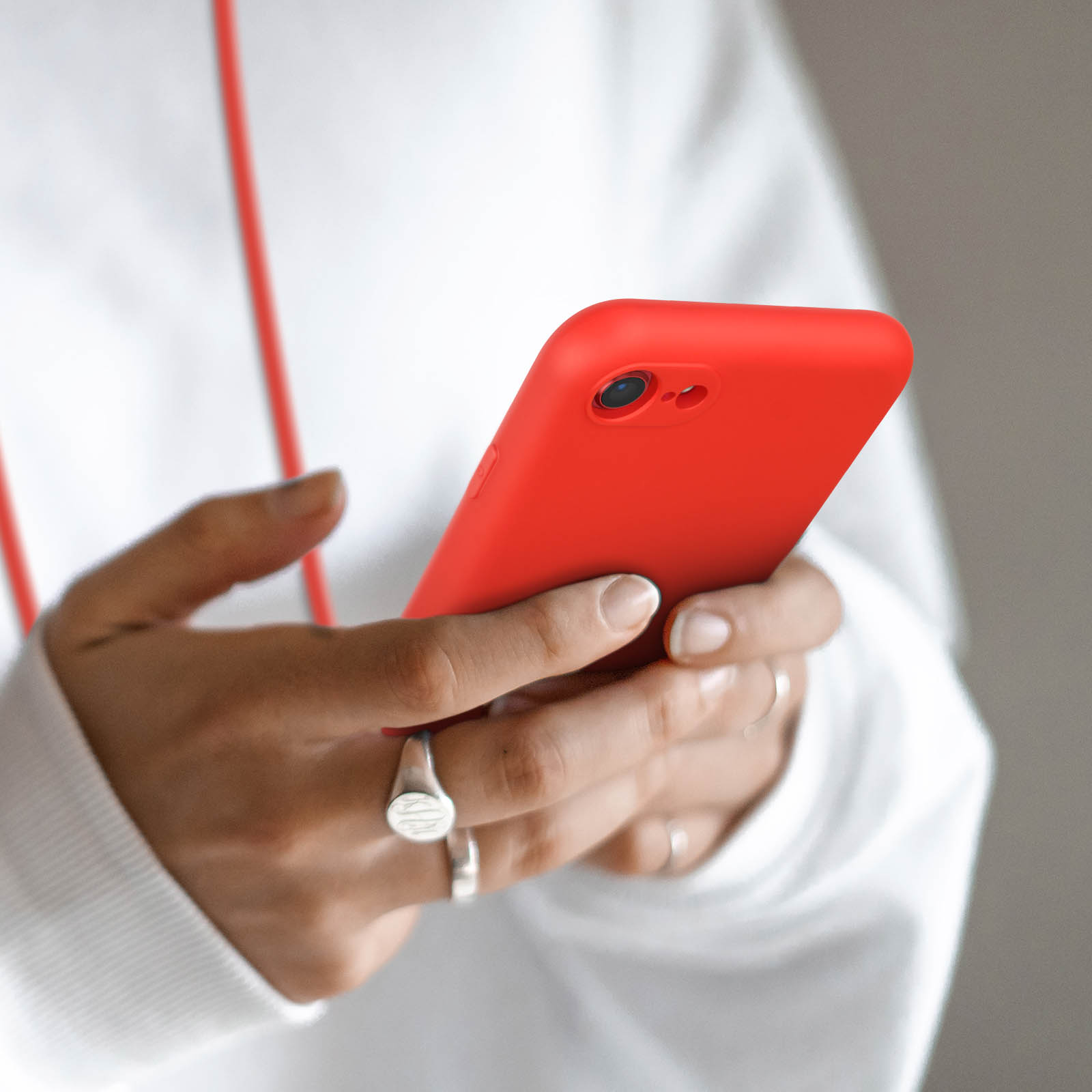Personne en sweat à capuche blanc tenant un smartphone rouge. Gros plan des mains avec bagues.