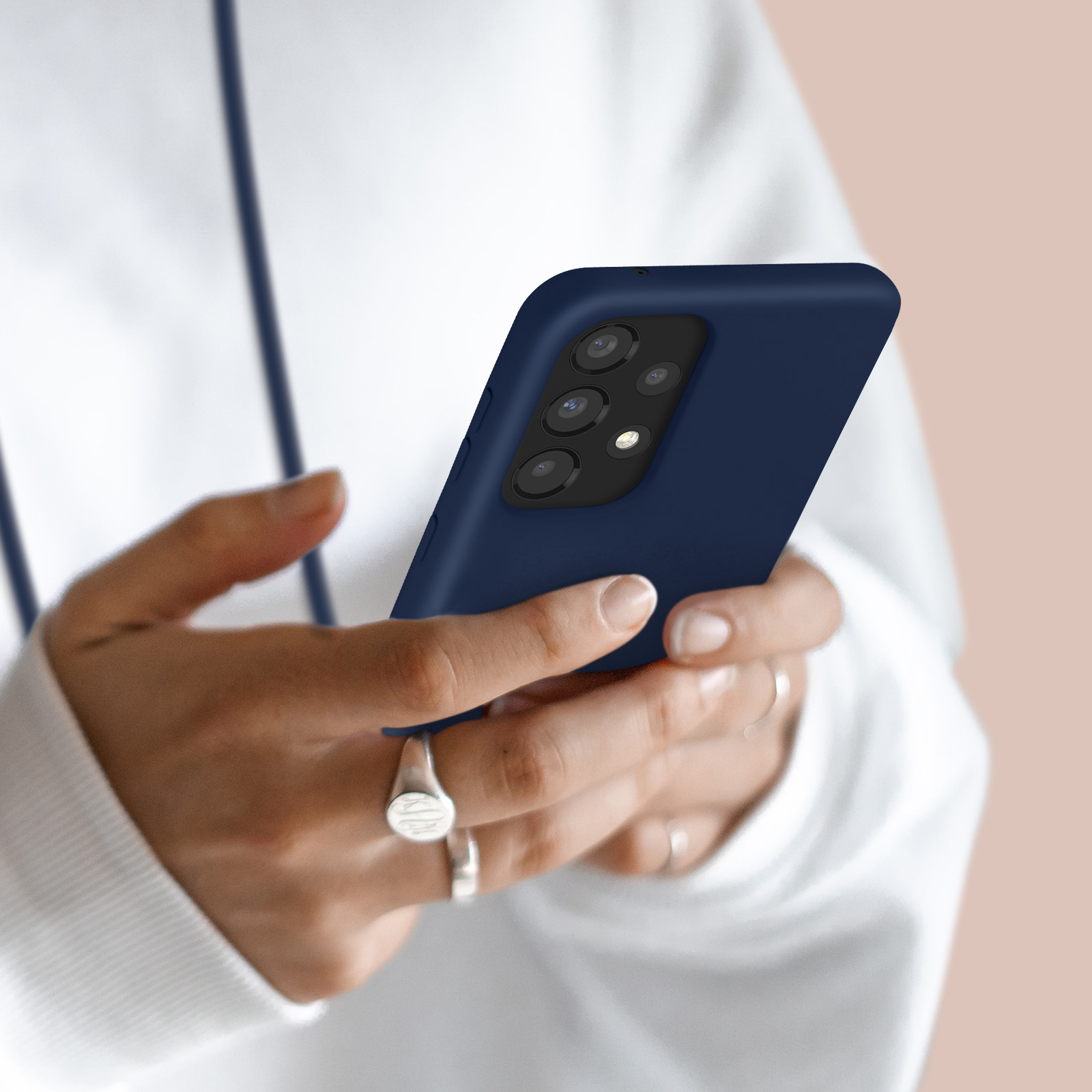 Personne en sweat à capuche blanc tenant un smartphone bleu foncé à quatre caméras.