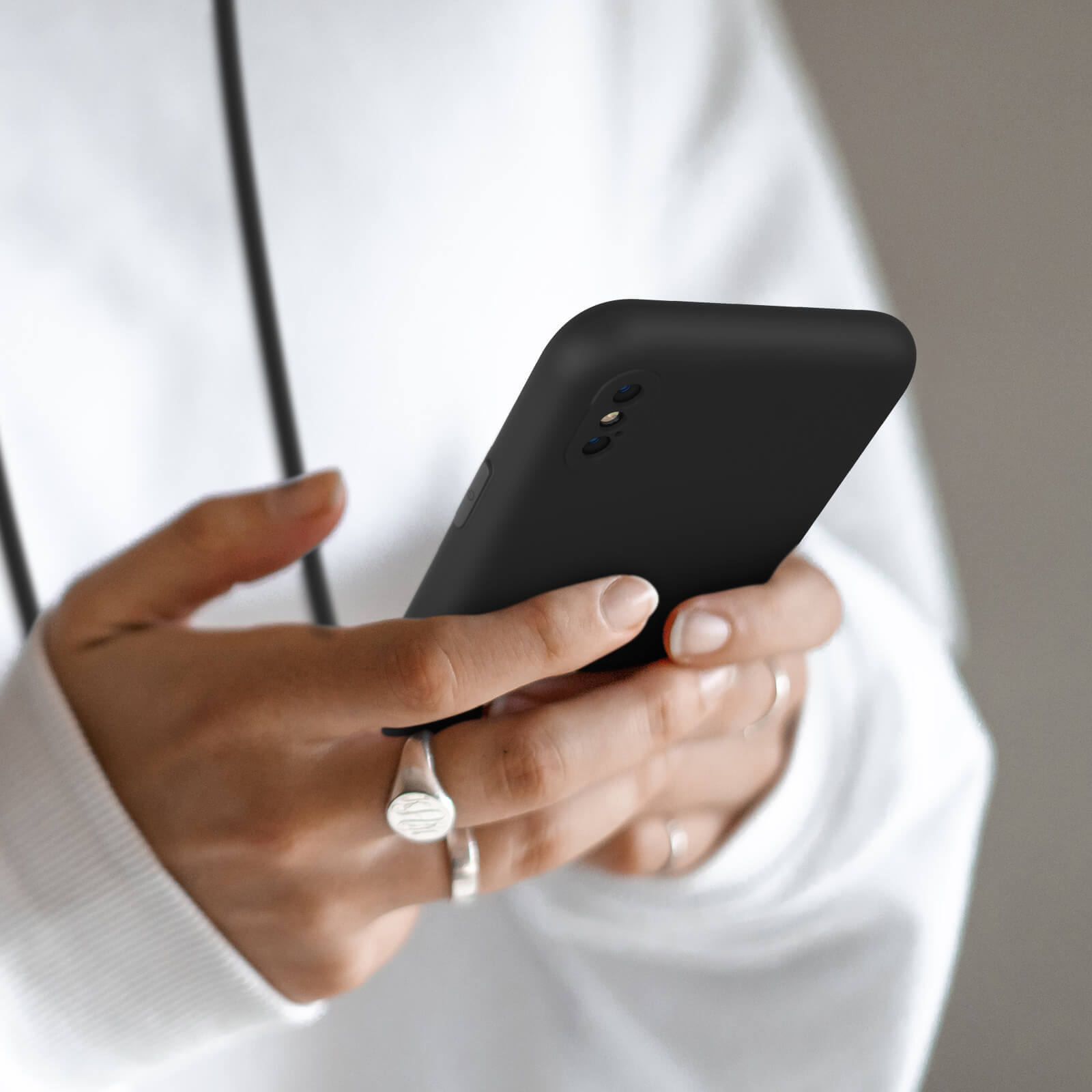 Une personne en sweat à capuche blanc tient un smartphone noir.