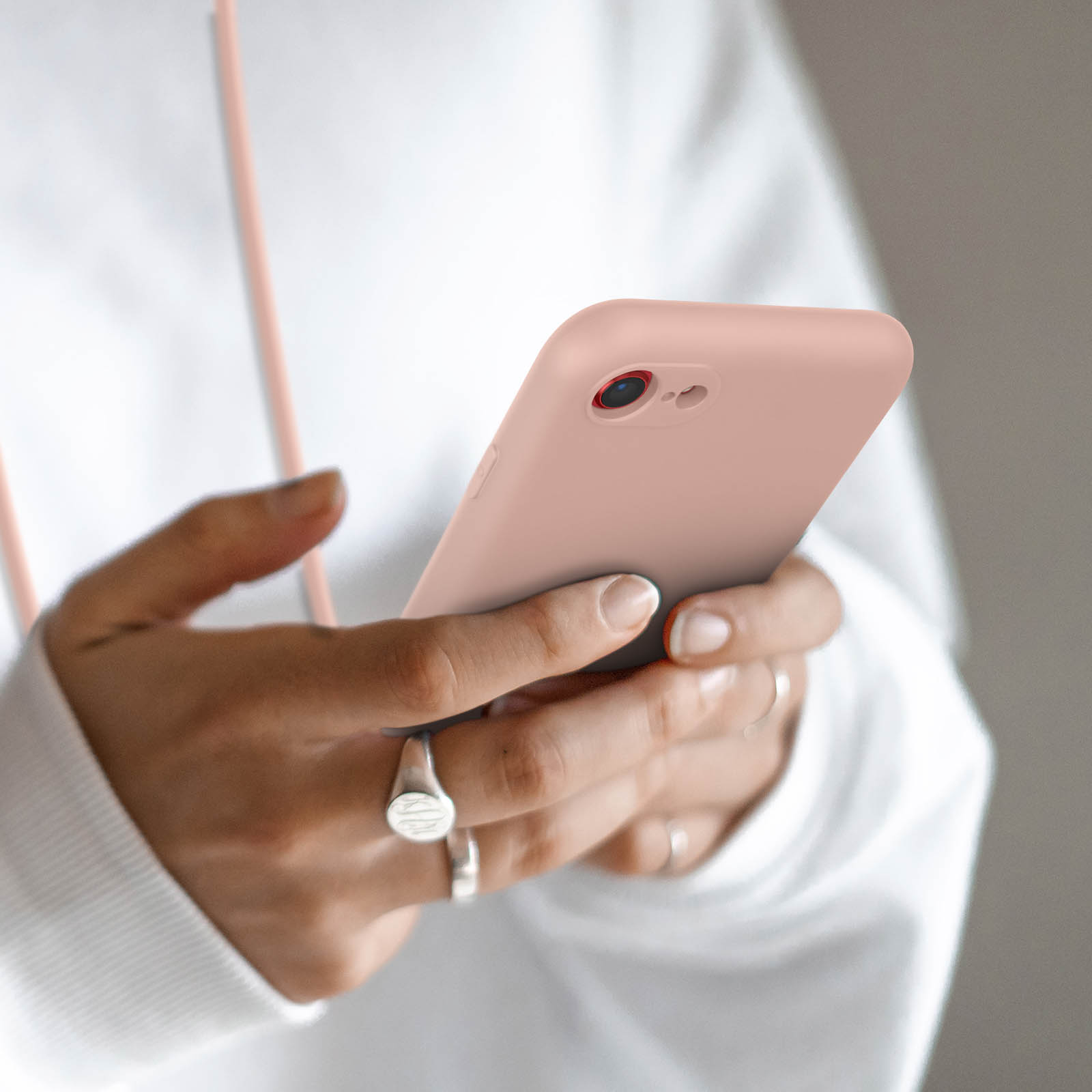 Une personne en sweat à capuche blanc tient un smartphone rose. Gros plan sur les mains.