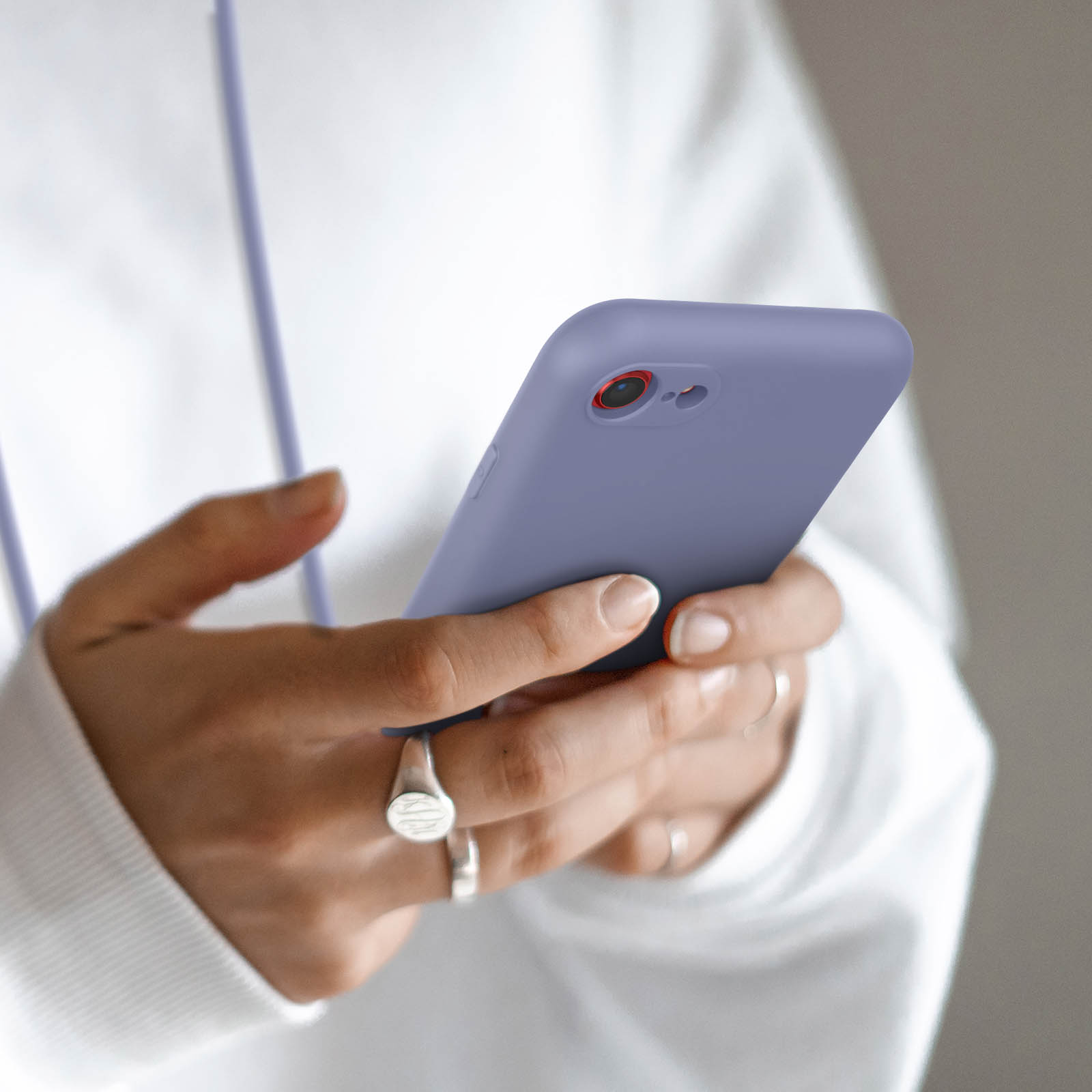 Personne tenant un smartphone violet avec des bagues aux doigts.