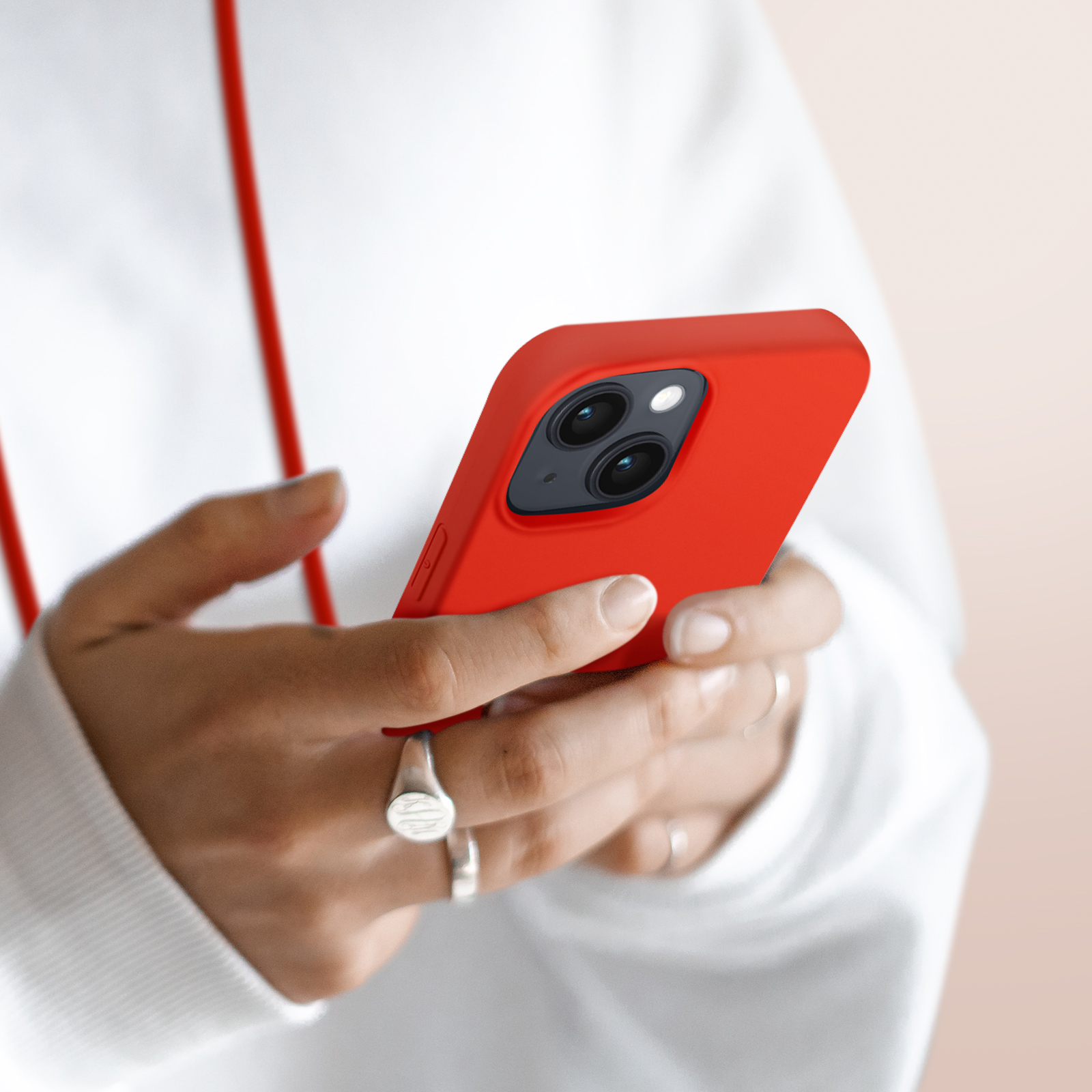 Handen houden een rode smartphone met twee camera's vast. Persoon draagt witte kleding.