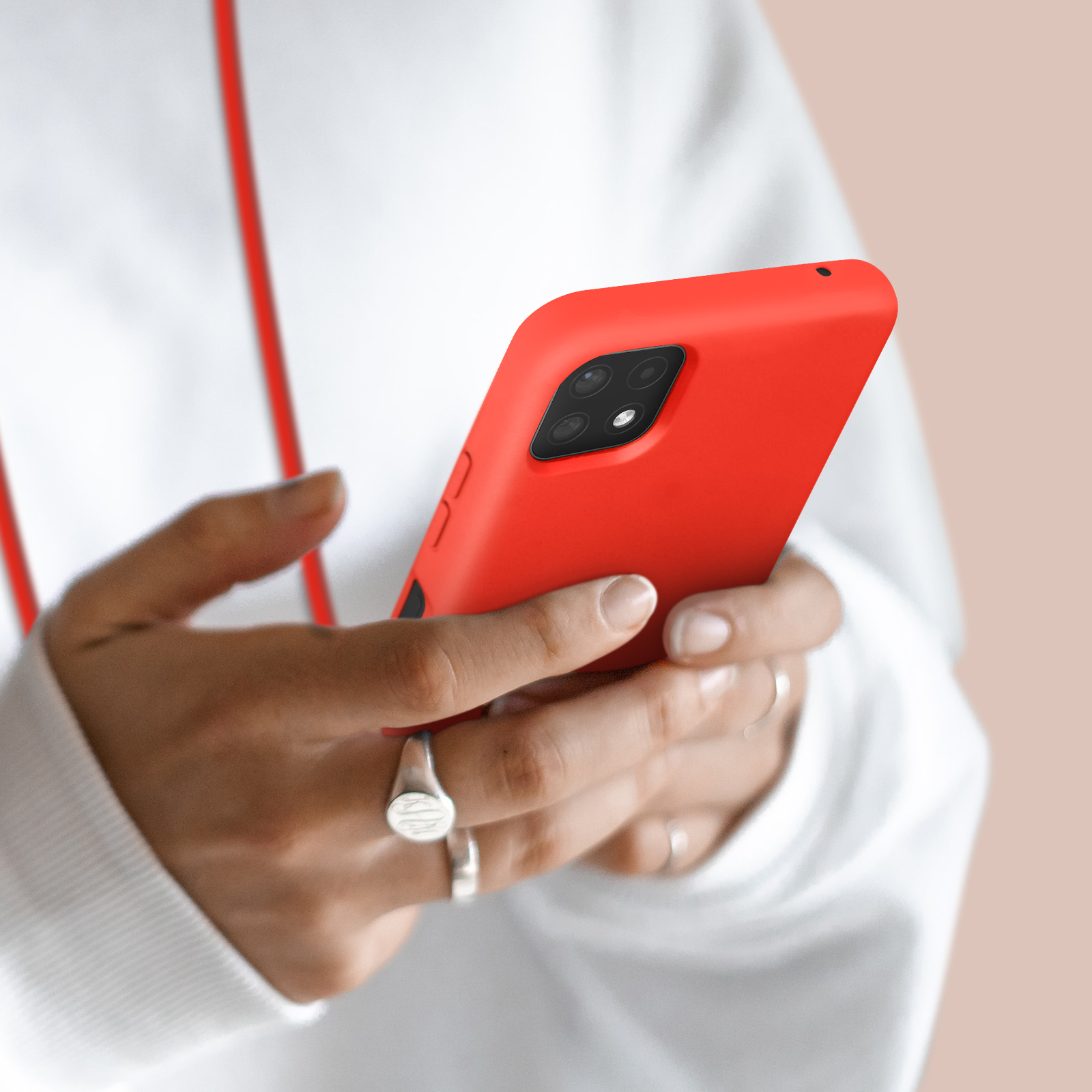 Une personne en sweat blanc tient un smartphone rouge à quatre caméras.