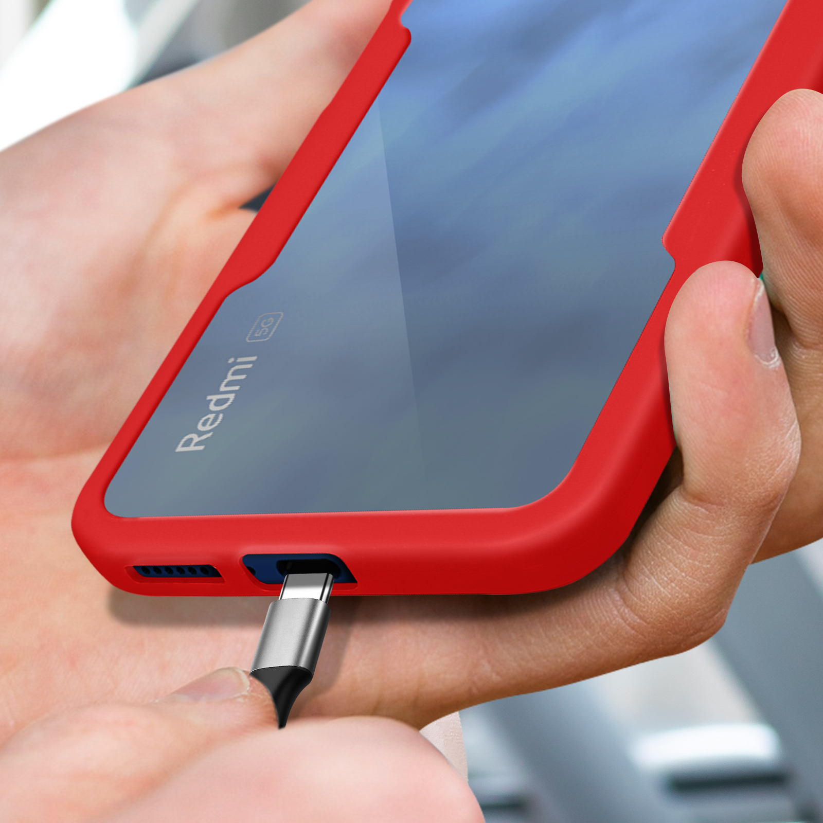Telefono rosso con cavo USB-C in fase di inserimento, tenuto dalle mani.