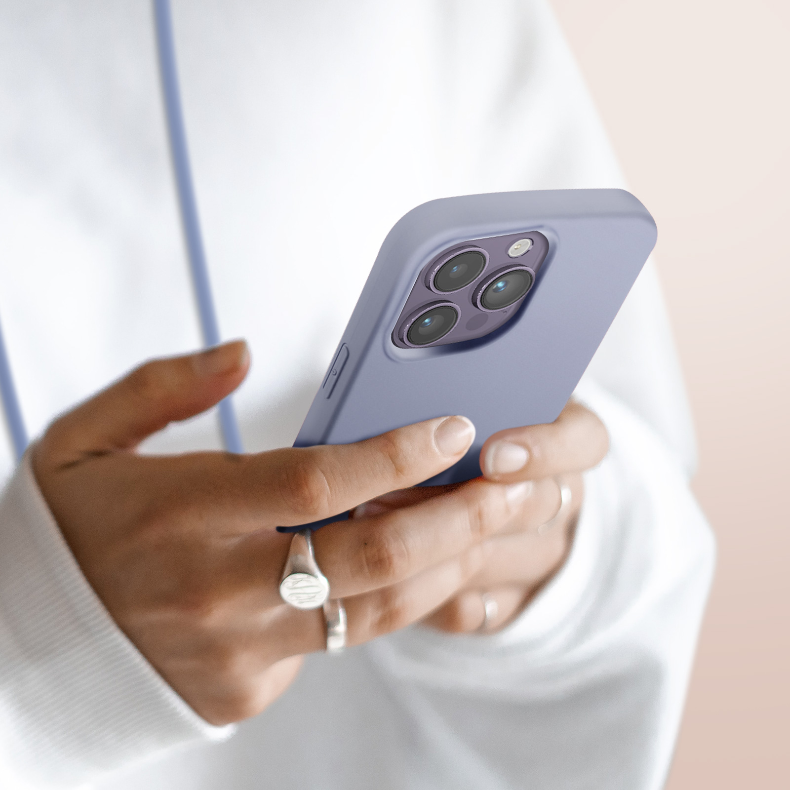 Une personne en sweat blanc tient un smartphone violet avec trois caméras.