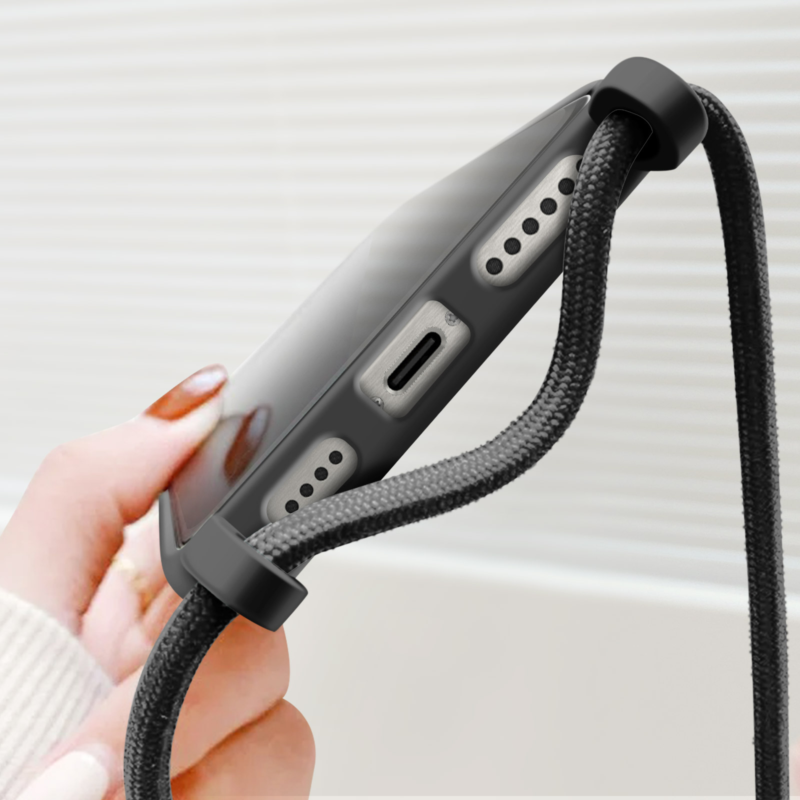 Mano che tiene telefono con laccetto nero. Pulsanti laterali e porta di ricarica visibili.