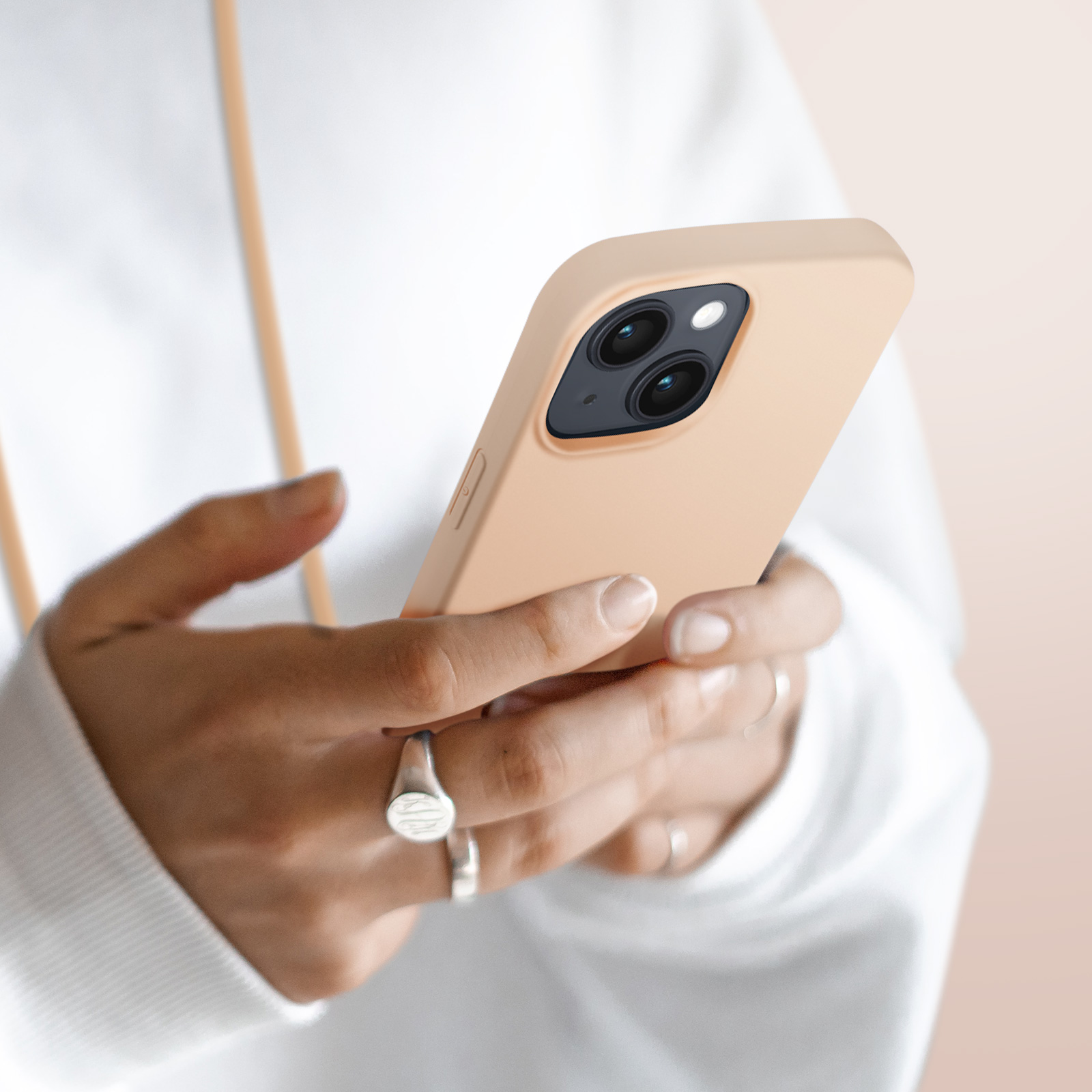 Handen houden een lichtbeige smartphone met dubbele camera vast.