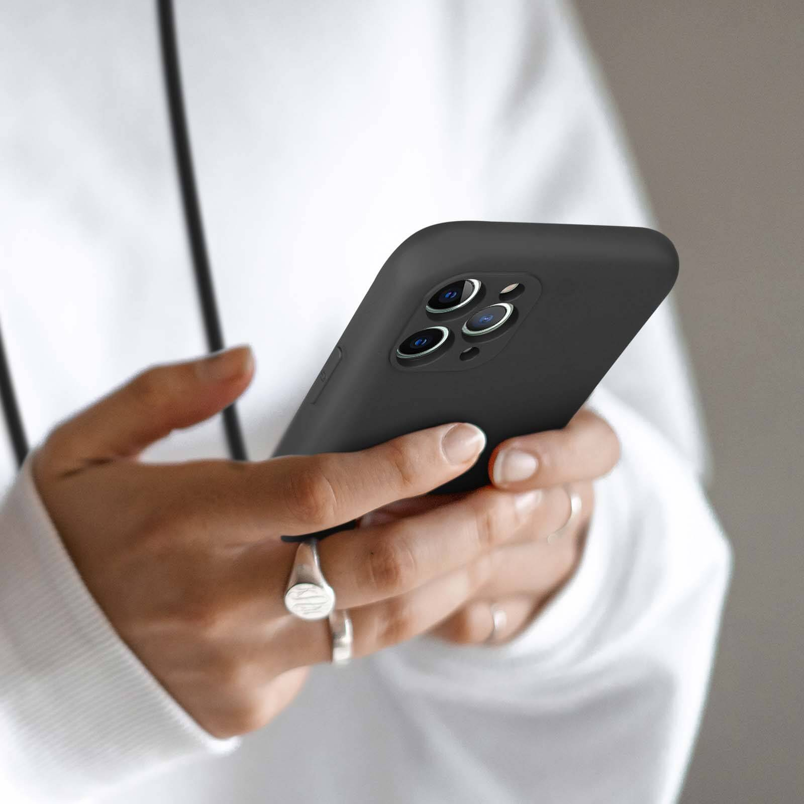Mains tenant un smartphone noir à trois caméras.