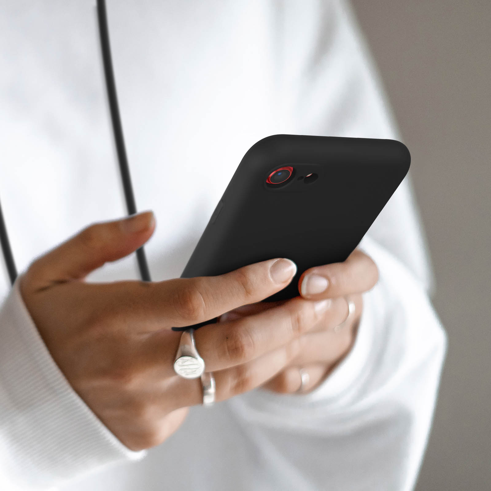 Personne en sweat à capuche blanc tenant un téléphone noir avec objectif de caméra rouge.