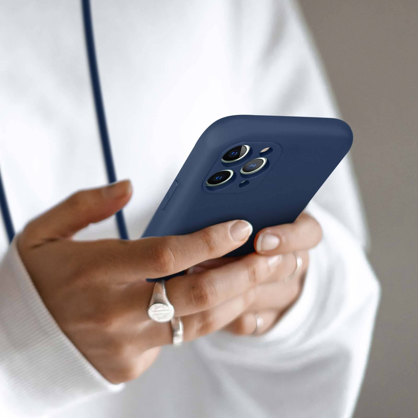 Une personne portant un sweat à capuche blanc tient un téléphone bleu foncé à trois caméras.