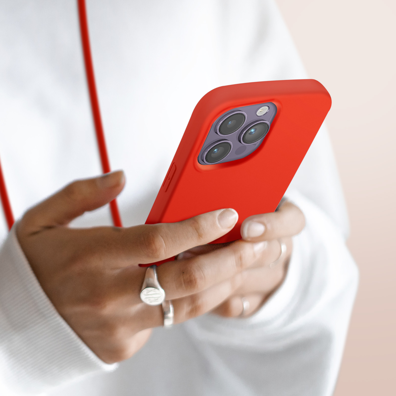 Mains tenant un smartphone rouge à trois caméras. Une personne porte des bagues.