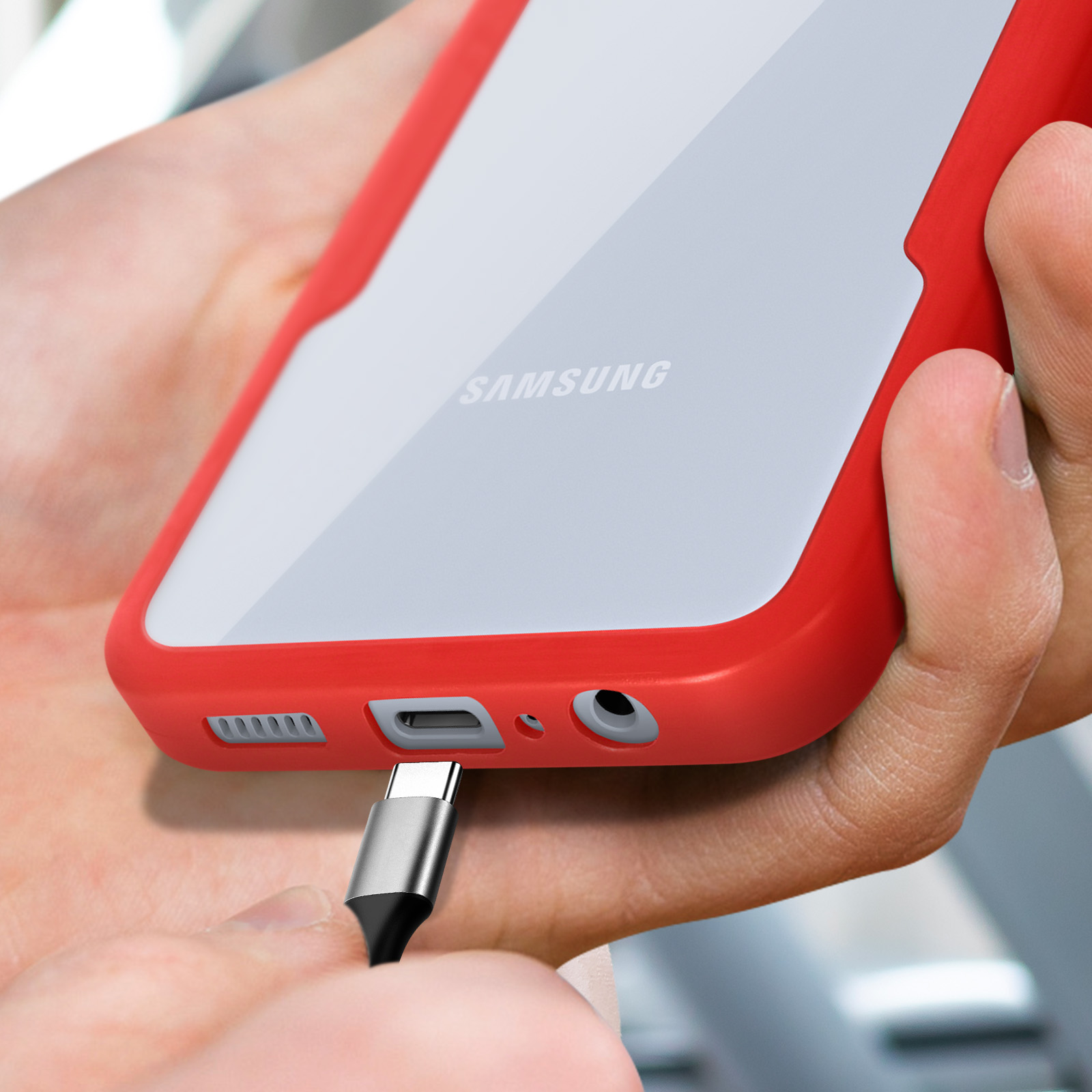 Un téléphone rouge tenu par des mains alors qu'un câble de chargement est branché.
