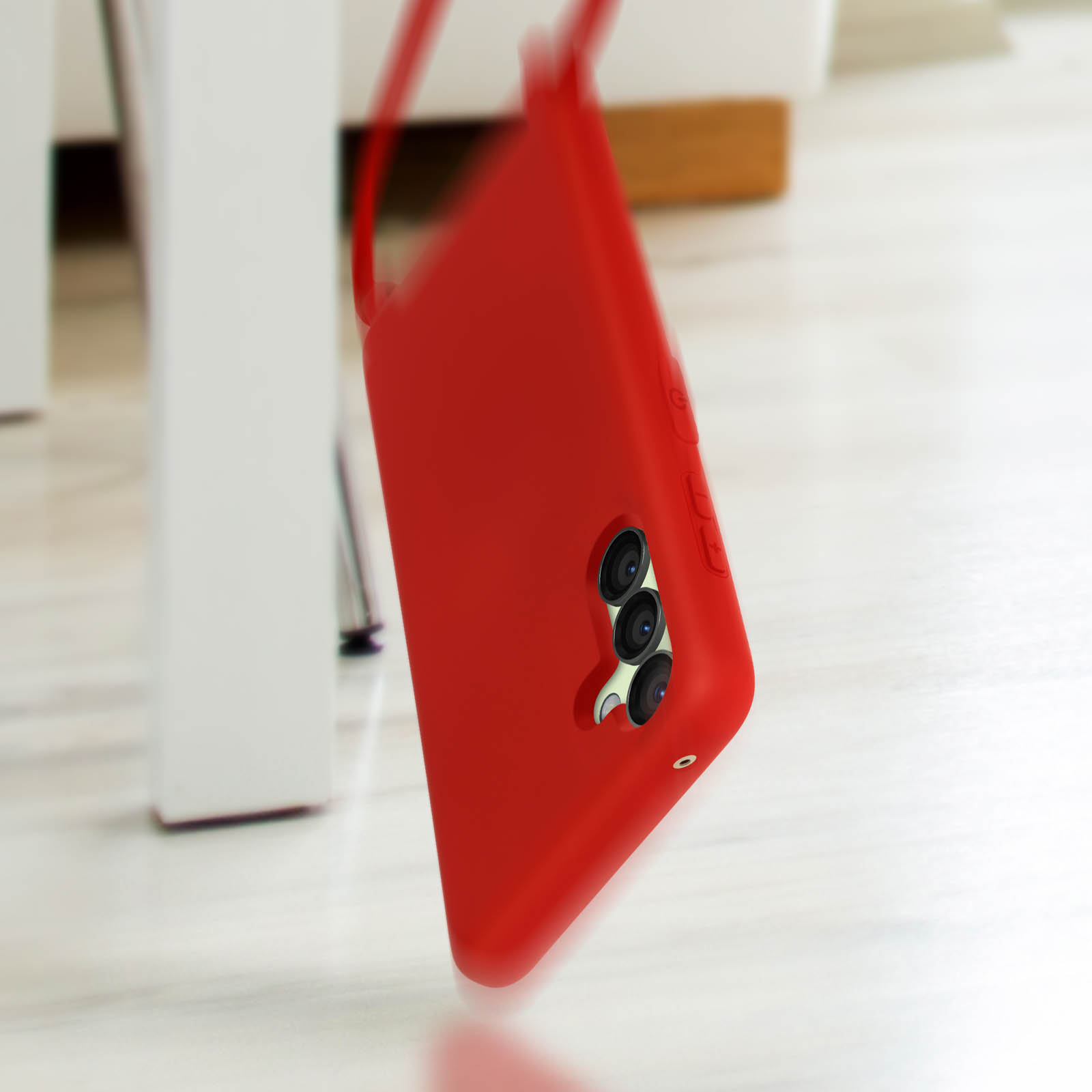 Una custodia rossa per telefono con tre fotocamere cade su un pavimento in legno.