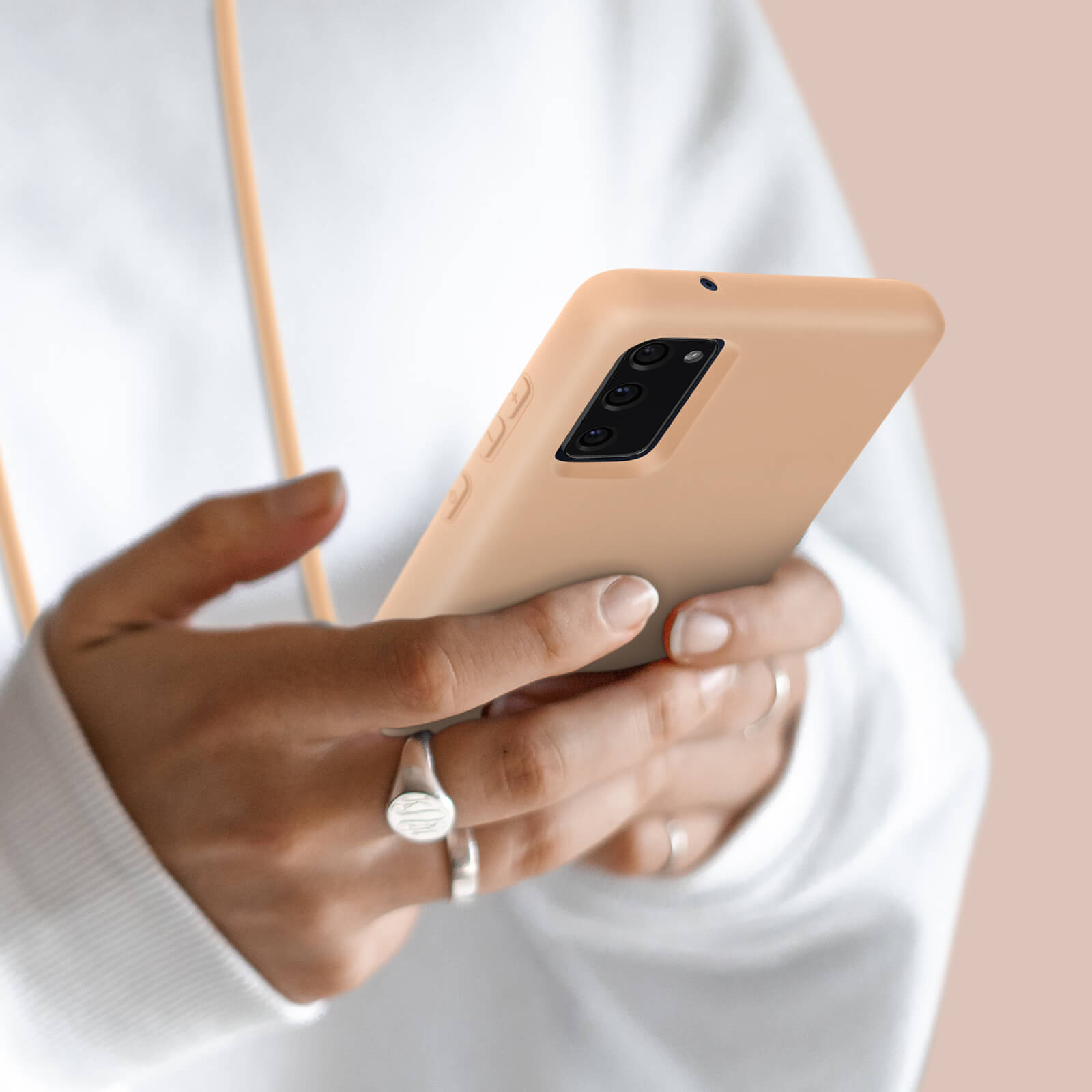 Mani che tengono uno smartphone color pesca chiaro con tre fotocamere.