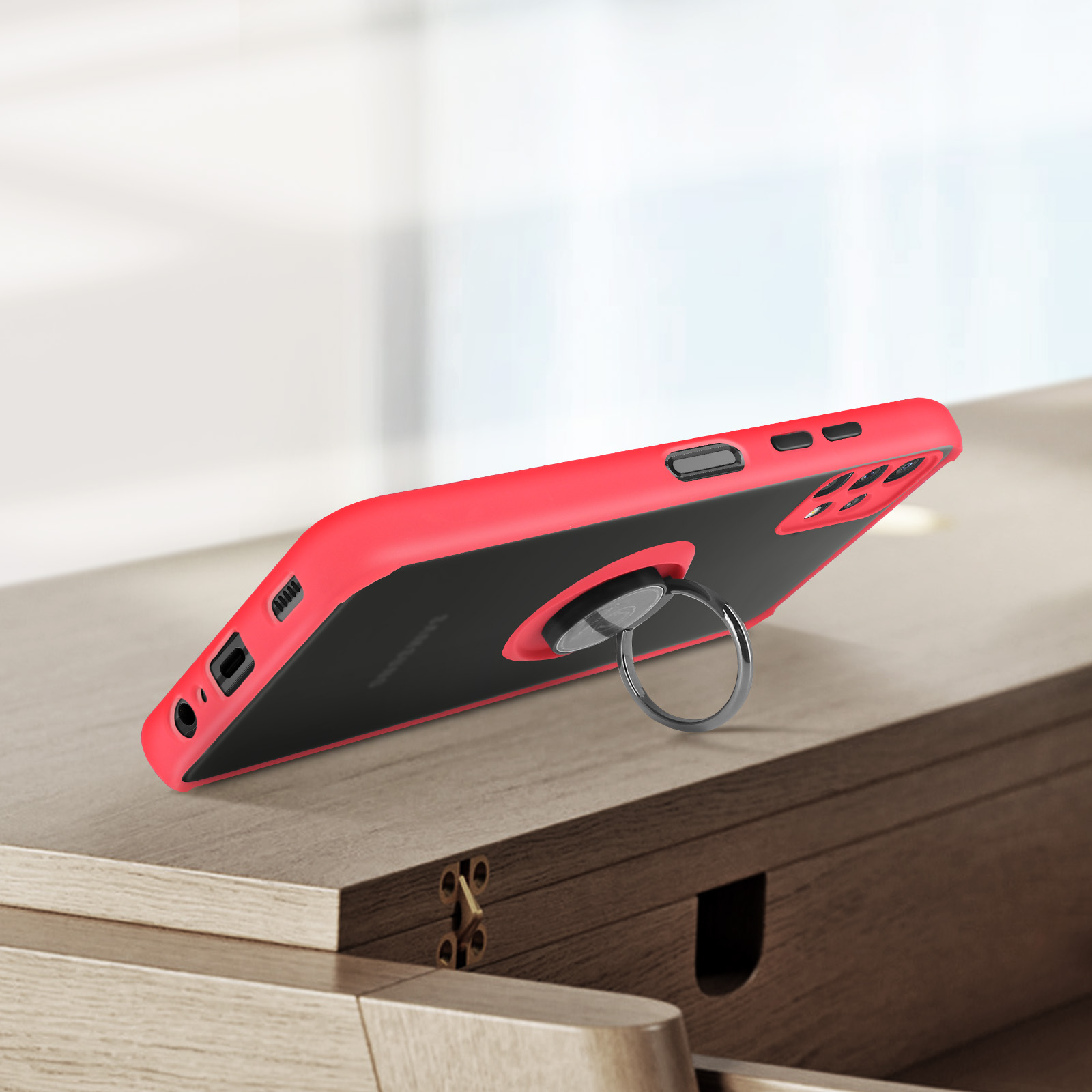 Rode telefoonhoes met zwarte transparante achterkant en zilveren ringhouder op houten tafel.