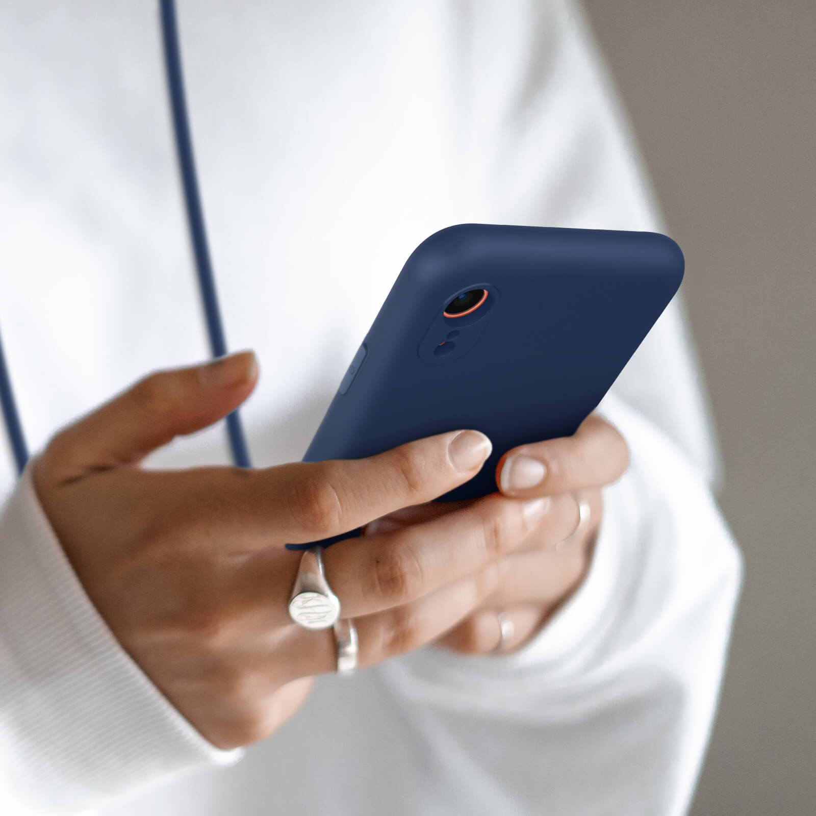 Mains tenant un téléphone bleu foncé avec des bagues et un sweat à capuche blanc.