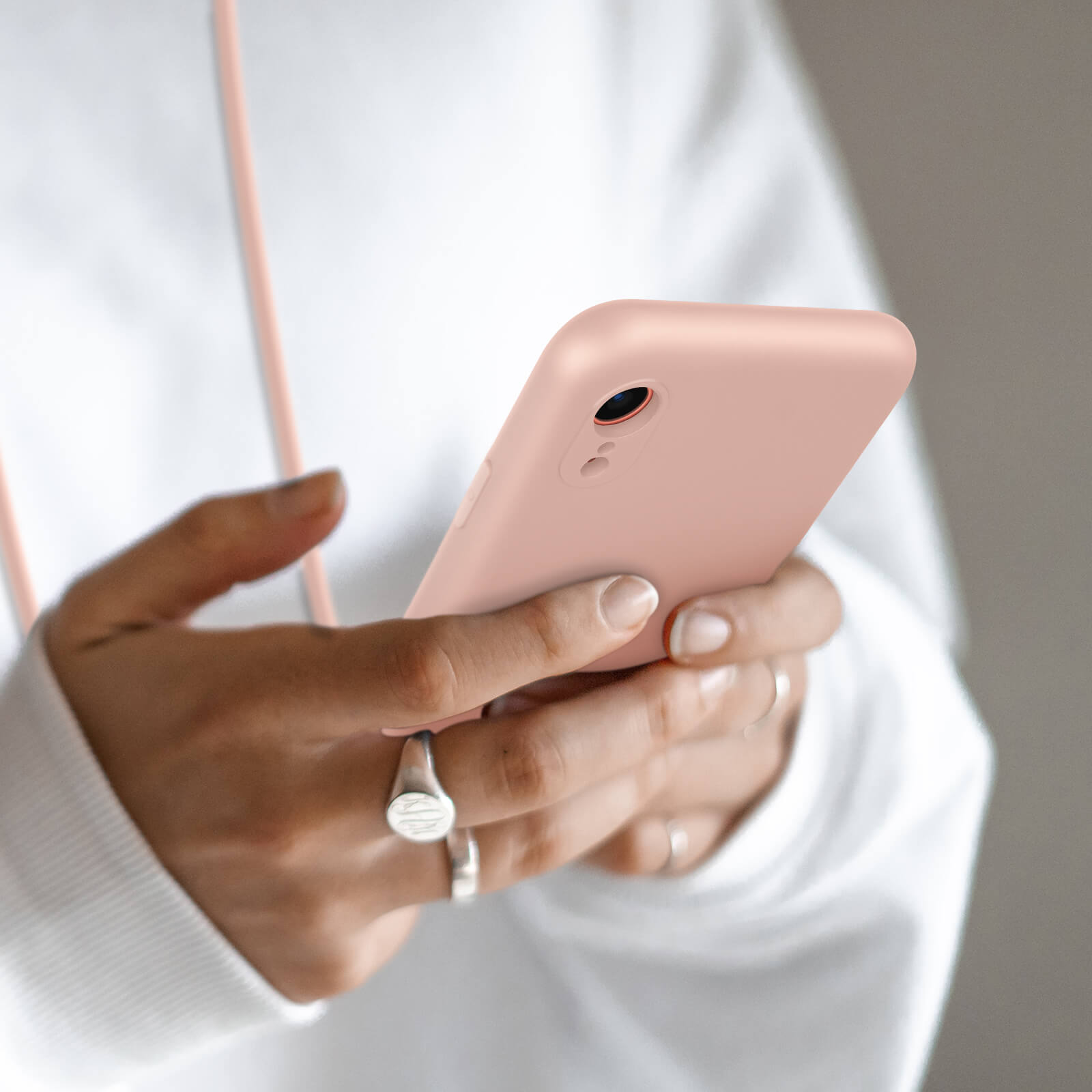 Une personne tenant un smartphone rose, portant un sweat à capuche blanc et des bagues.