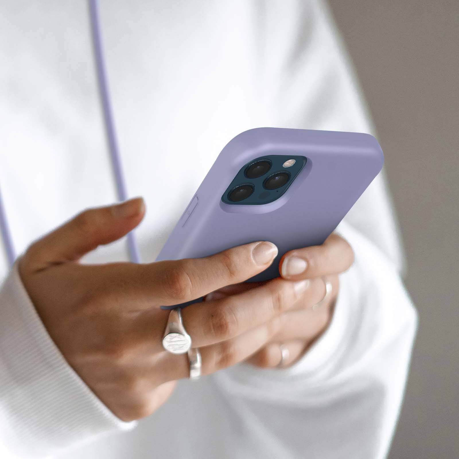 Mains tenant un iPhone violet avec trois caméras. Plusieurs bagues sont visibles.