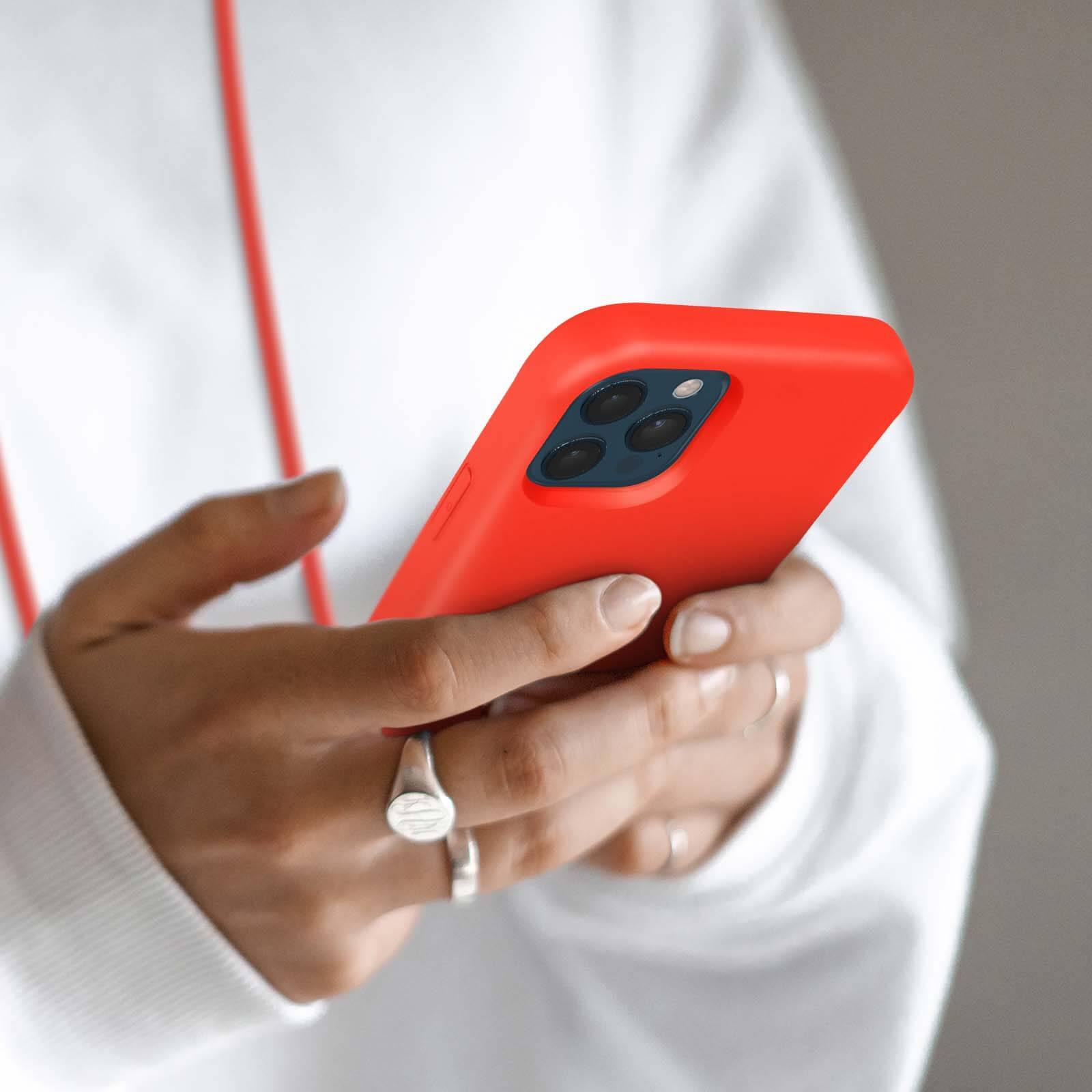 Een persoon houdt een rode iPhone met drie camera's vast.