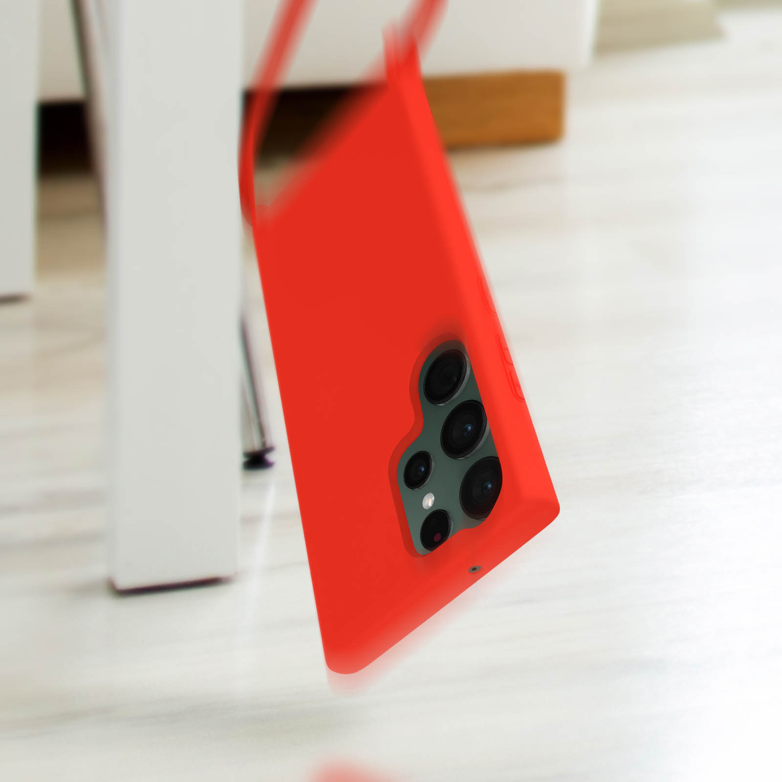 Una cover rossa per telefono con fotocamere che cade, oggetti bianchi sullo sfondo.