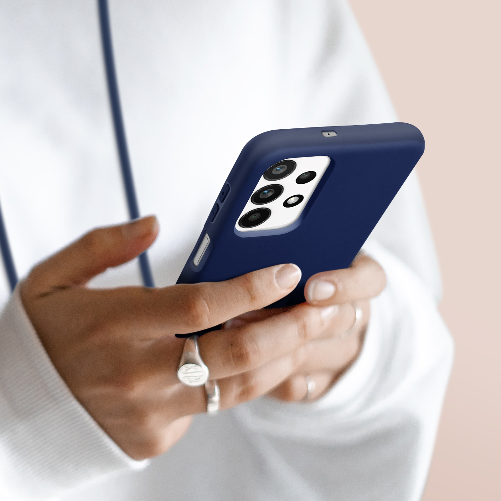 Personne en sweat à capuche blanc tenant un smartphone bleu foncé avec module caméra.