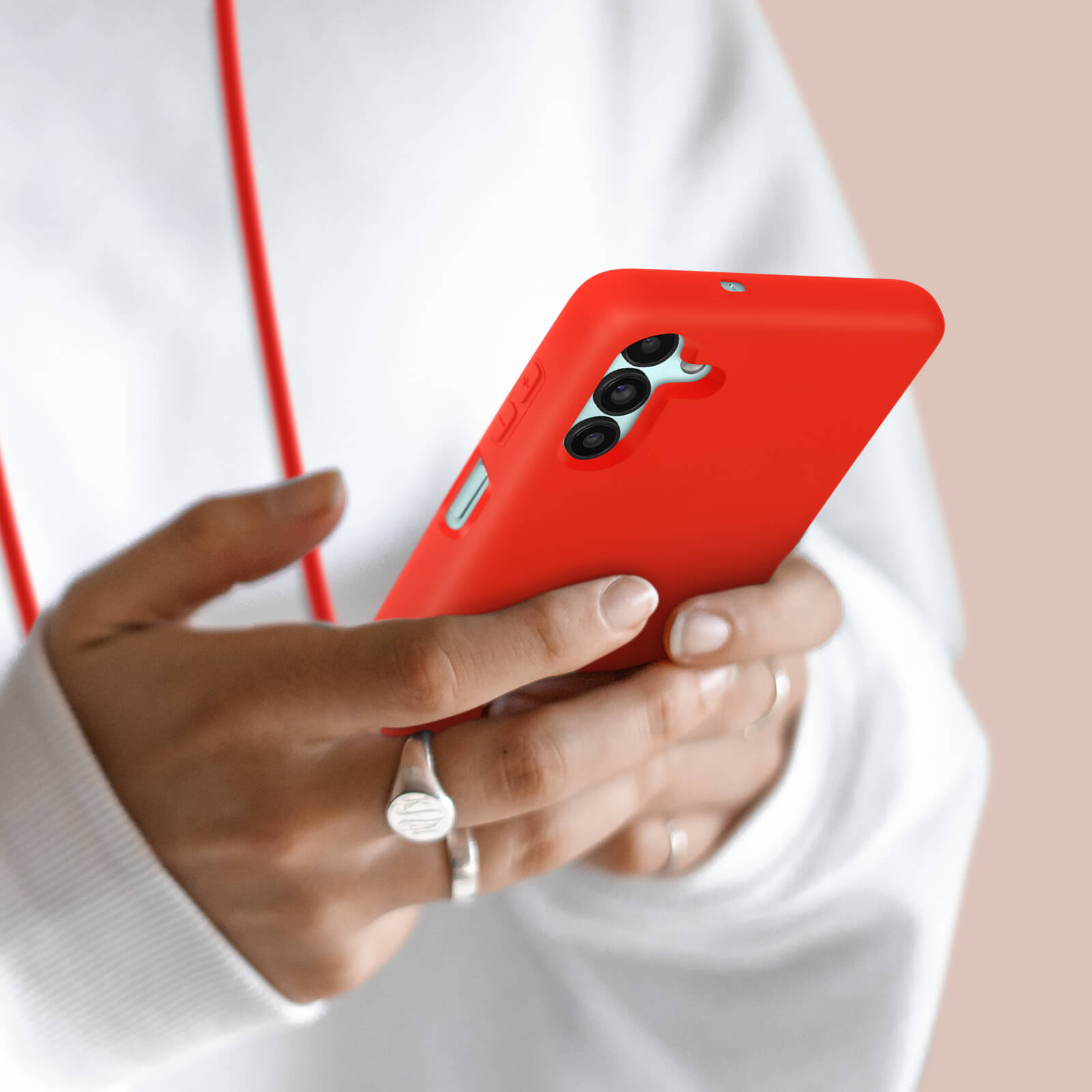 Persoon houdt een rode smartphone met drie camera's vast. Witte hoodie.