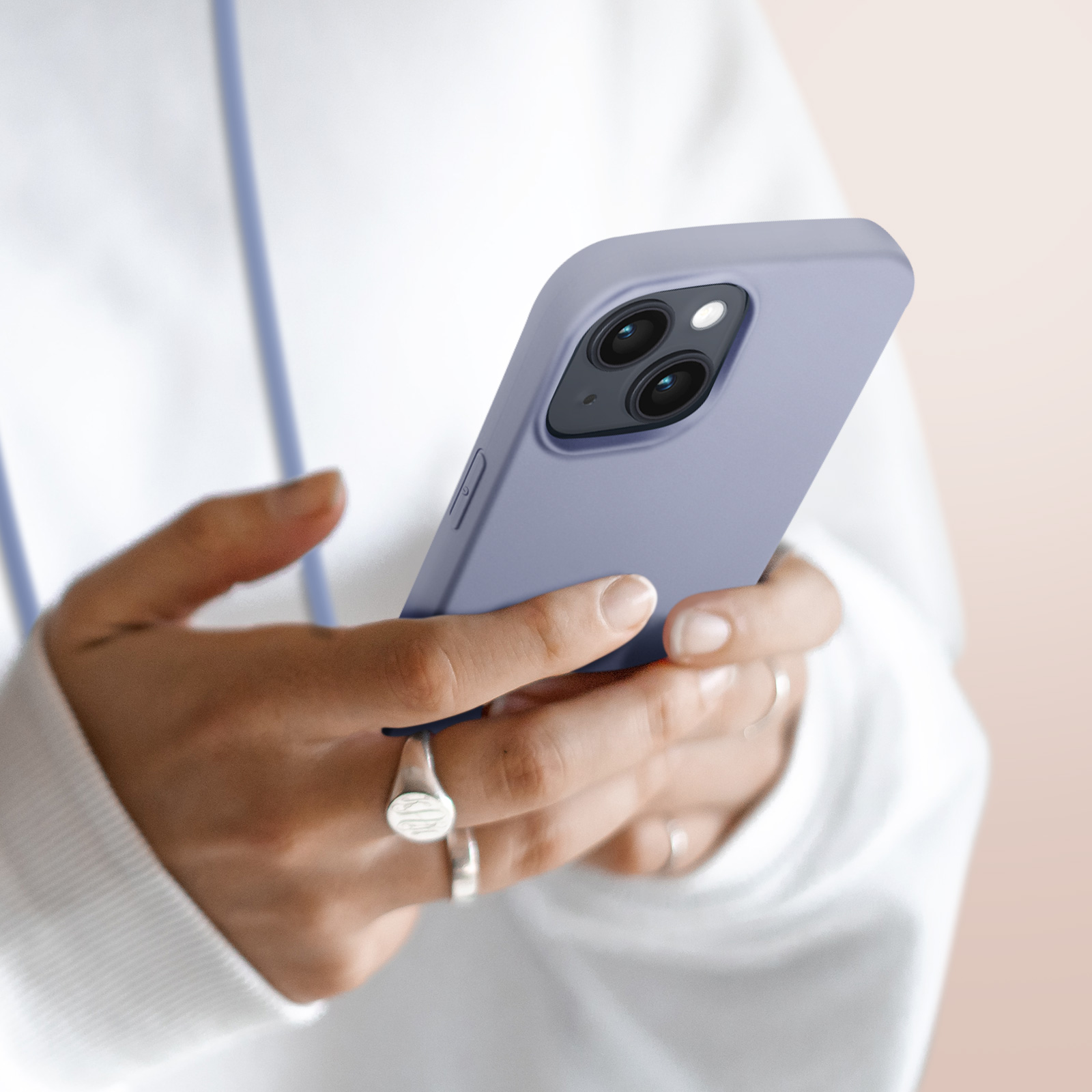 Een hand houdt een paarse iPhone met twee camera's vast. Vingers met ringen.