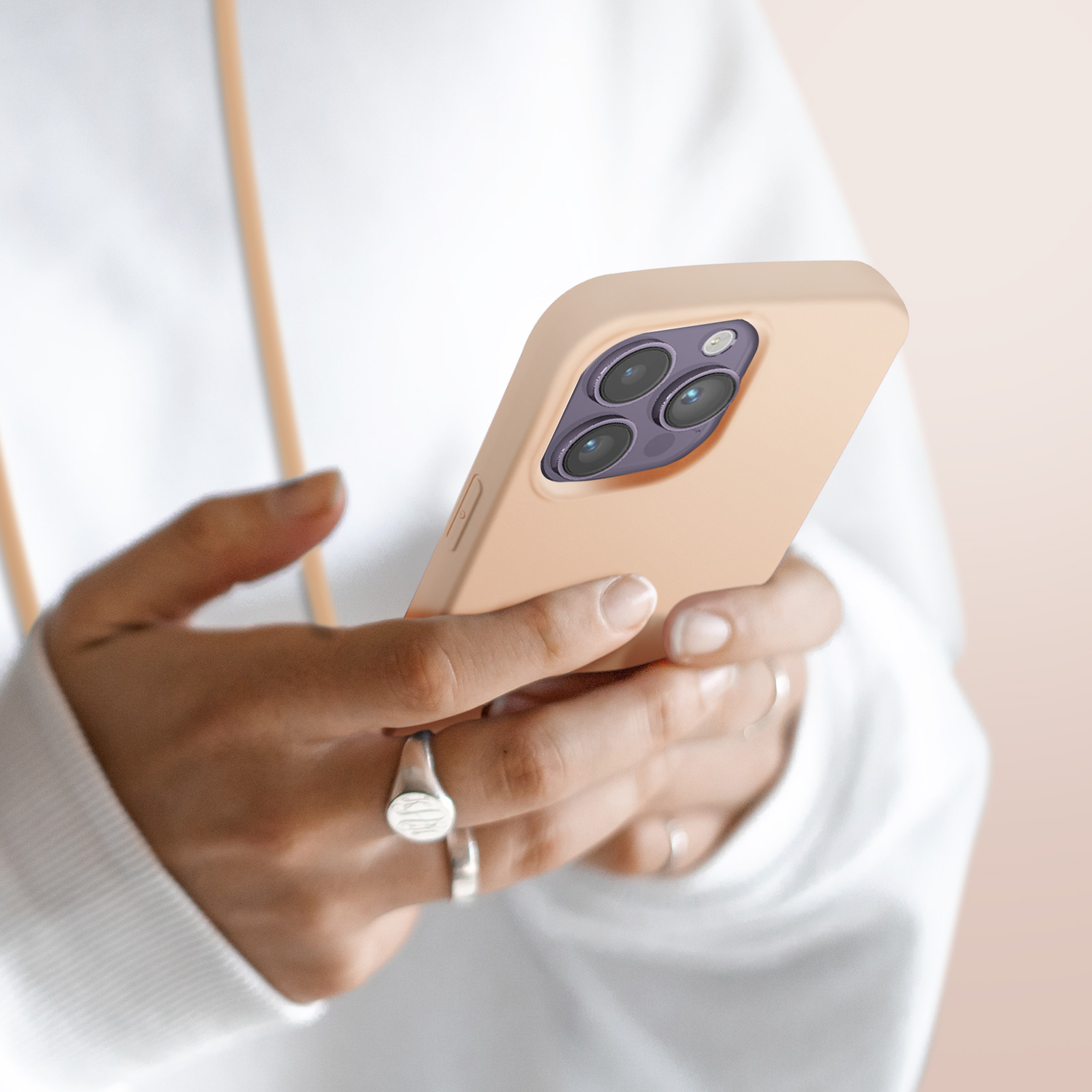 Een persoon houdt een licht perzikkleurige smartphone met drie cameralenzen vast.
