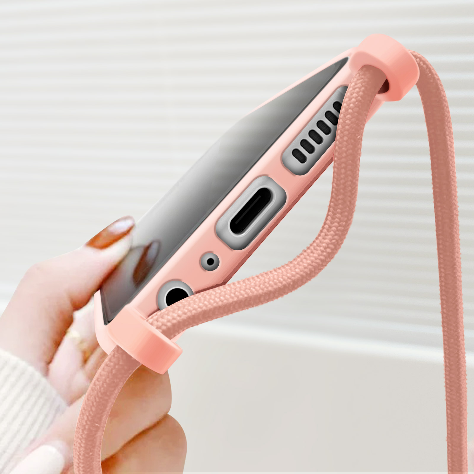 Une main tient un téléphone rose avec une dragonne et un port de charge.