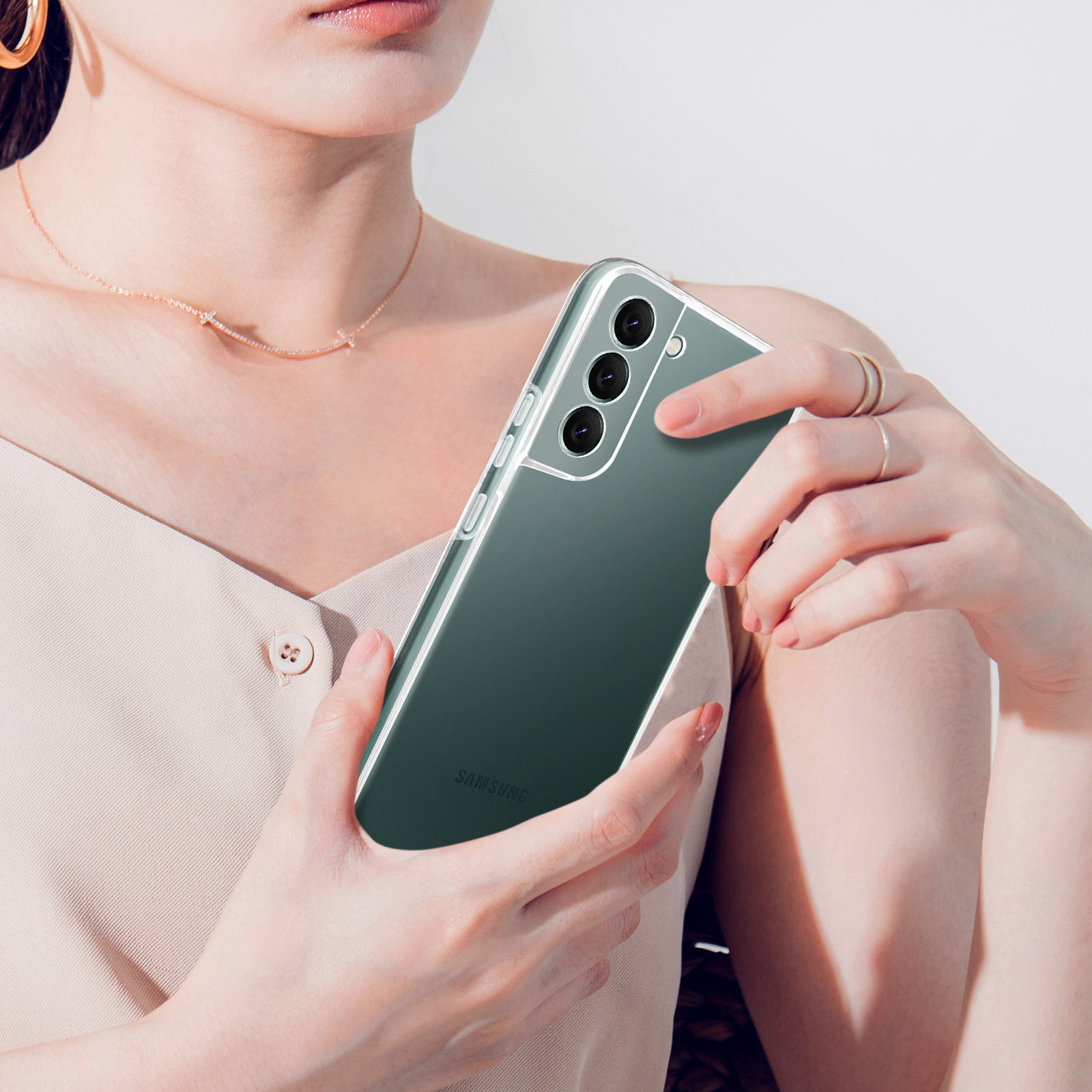 Une femme tient un smartphone vert dans un étui transparent, montrant trois caméras.