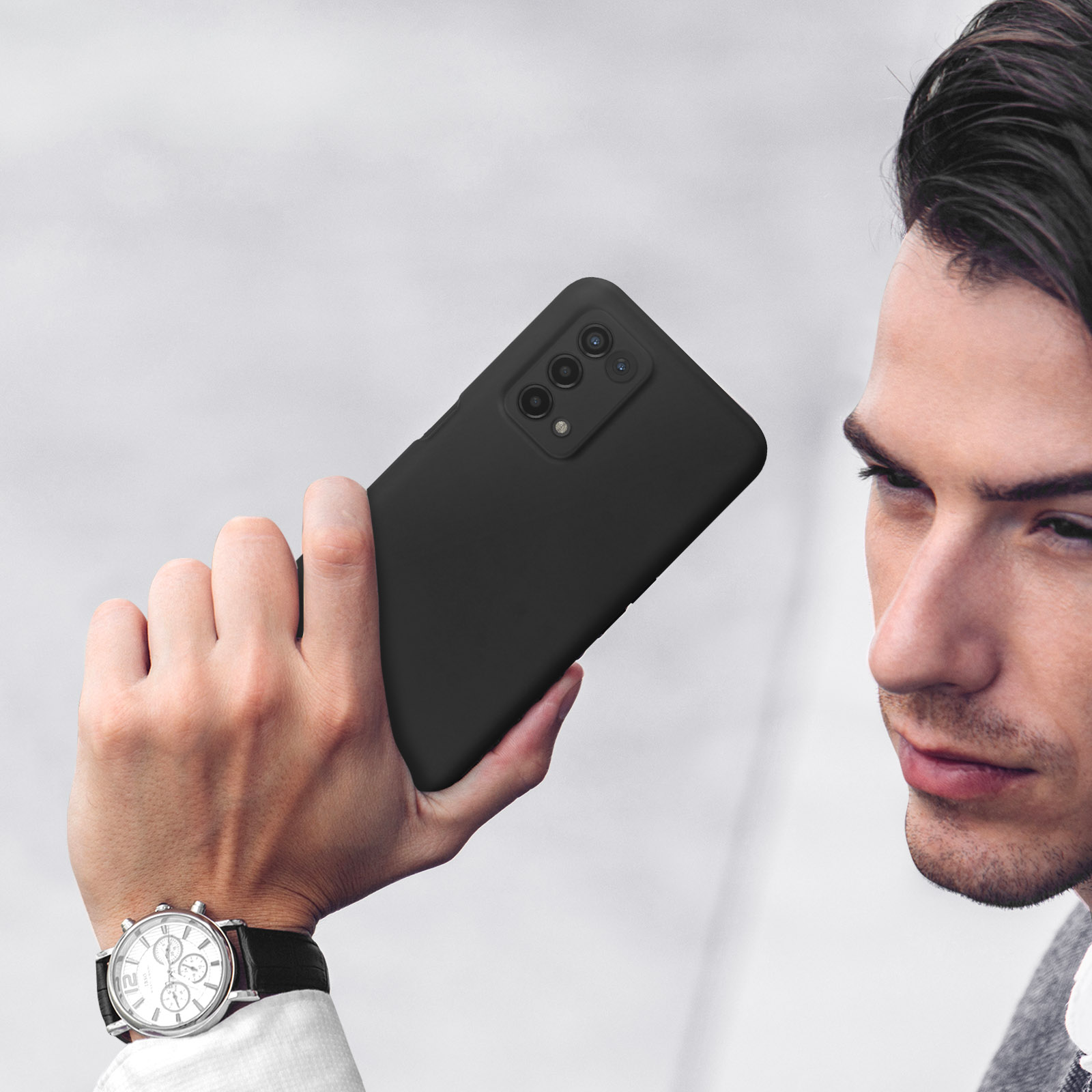Homme tenant un smartphone noir avec trois caméras. Montre au poignet.