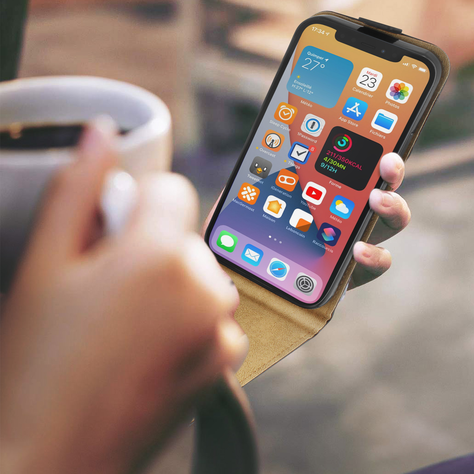 Una mano tiene un iPhone con molte icone di app. Una tazza di caffè è vicina.