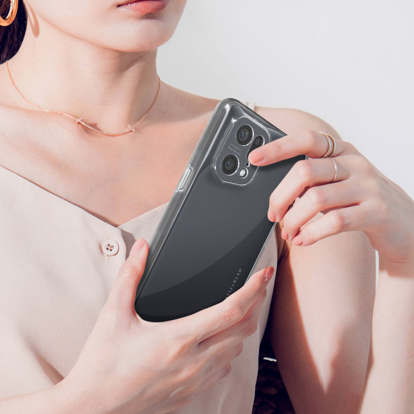 Een vrouw met een doorzichtige telefoonhoes houdt een smartphone vast. Ze draagt sieraden.